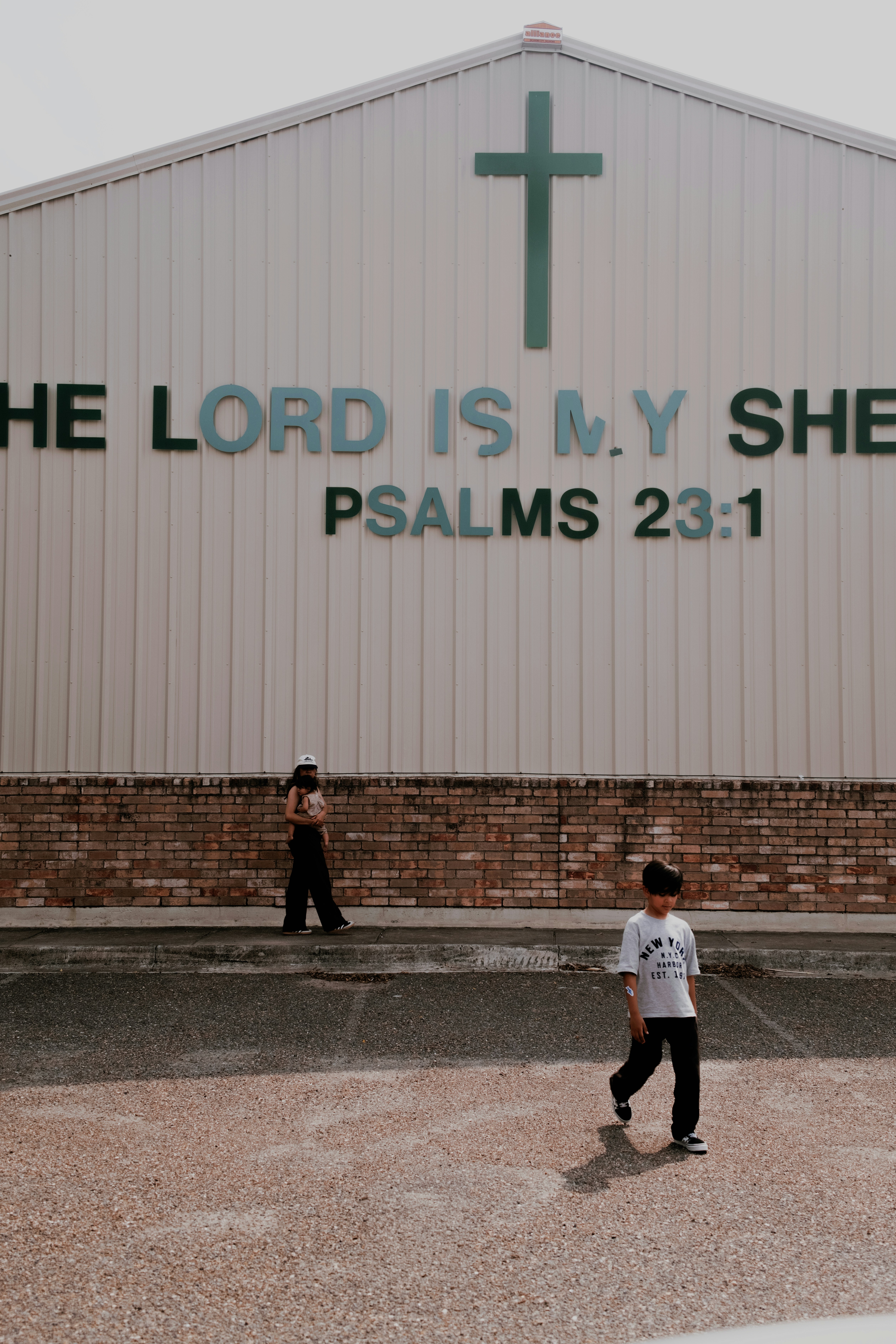 A person carrying a child and a boy walking past a church wall