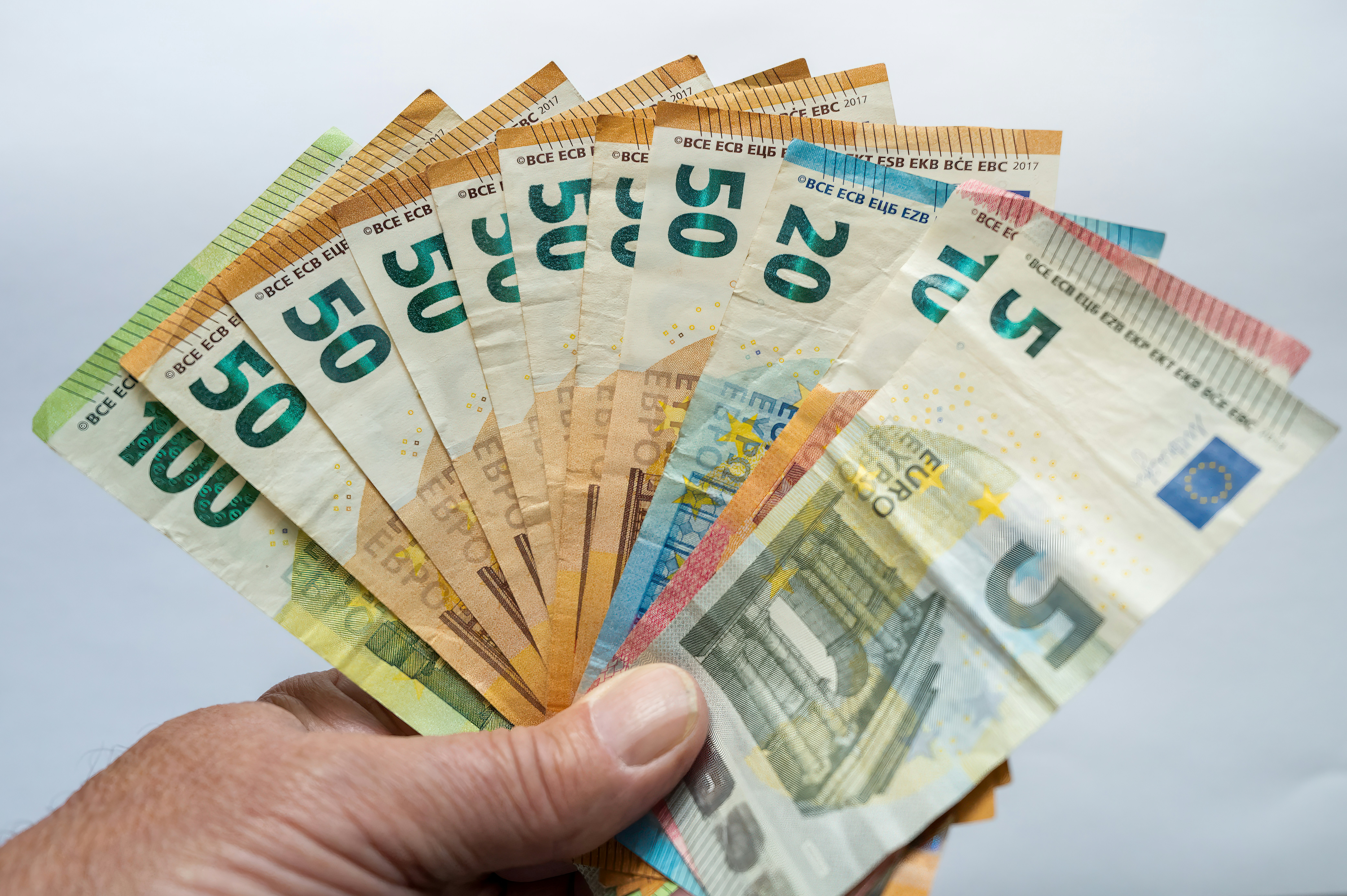 A hand holding a fan of assorted euro banknotes against a plain background