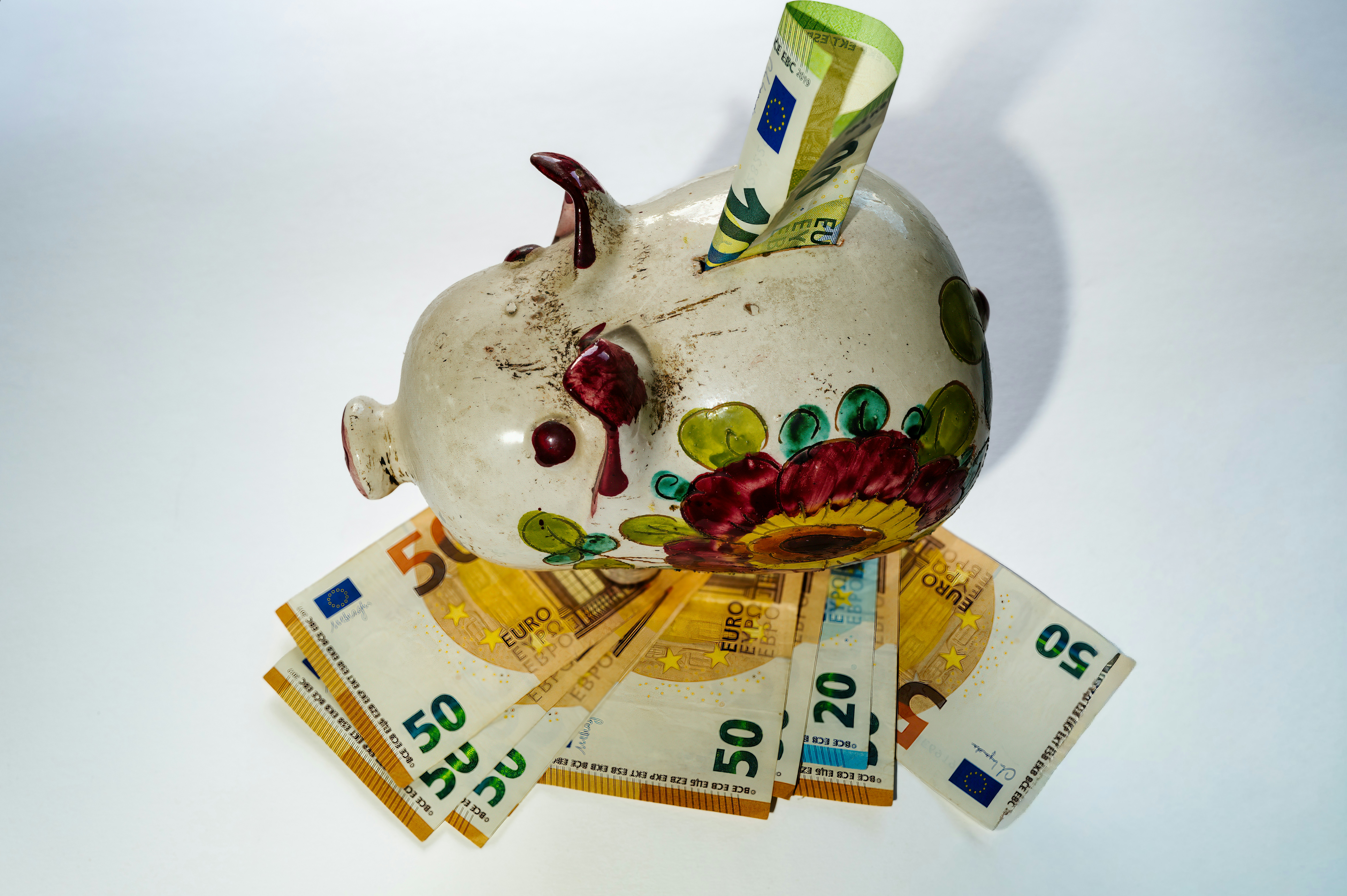 A ceramic piggy bank with floral patterns resting on a fan of euro banknotes