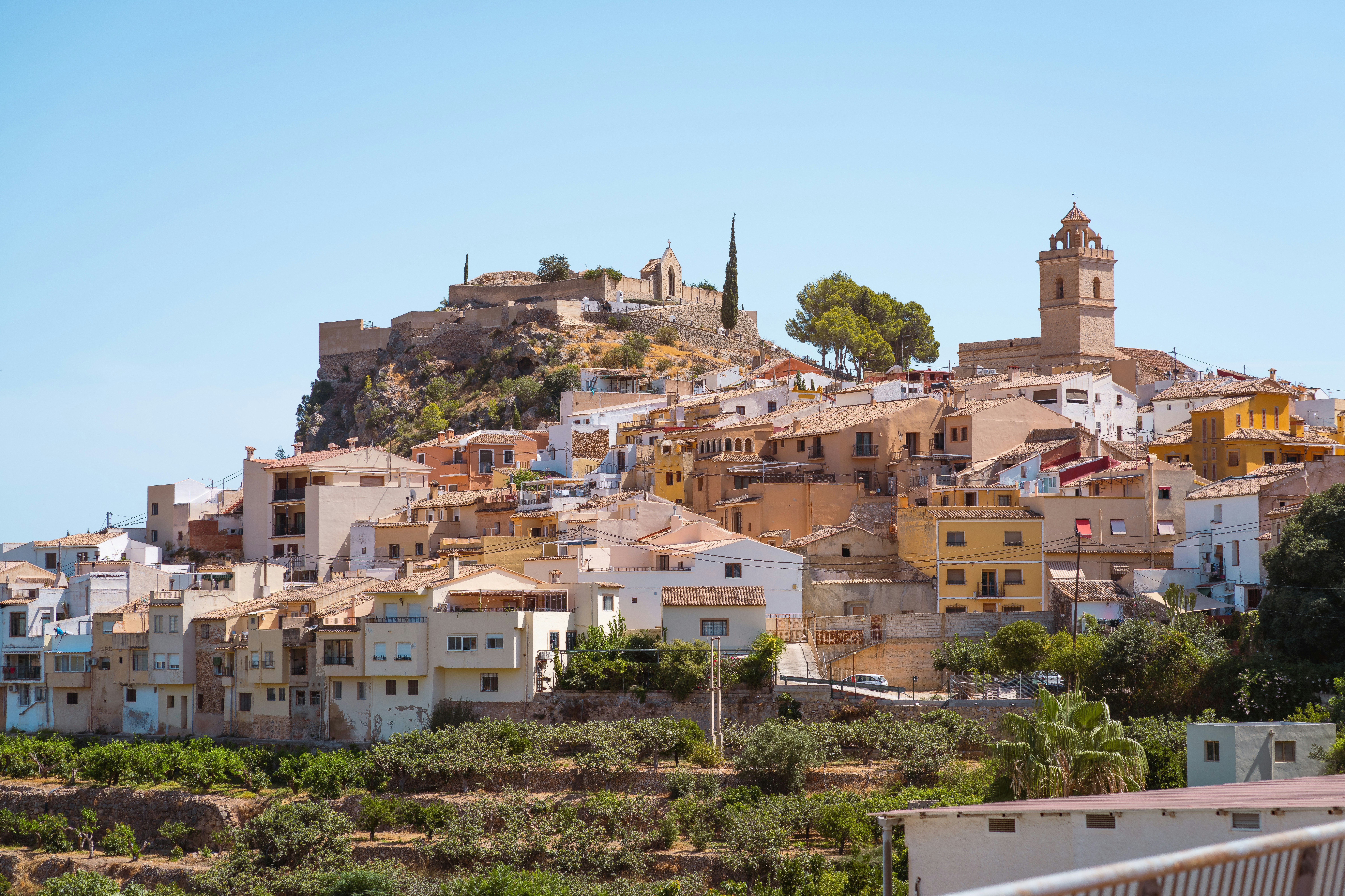 A hillside village with terracotta roofs and a stone church under a clear sky