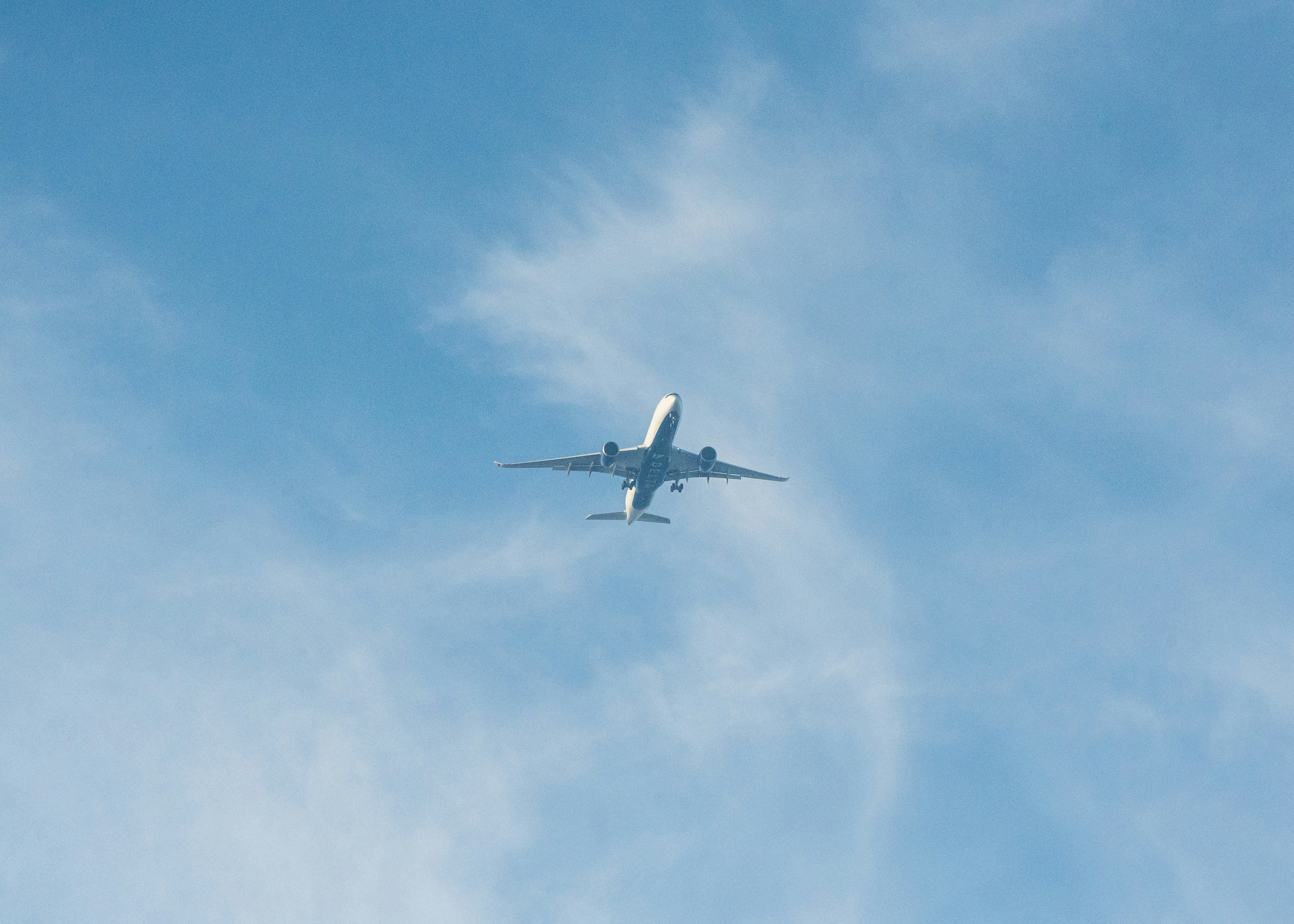 明るい青空を飛ぶ旅客機が、薄い白い雲を舞う