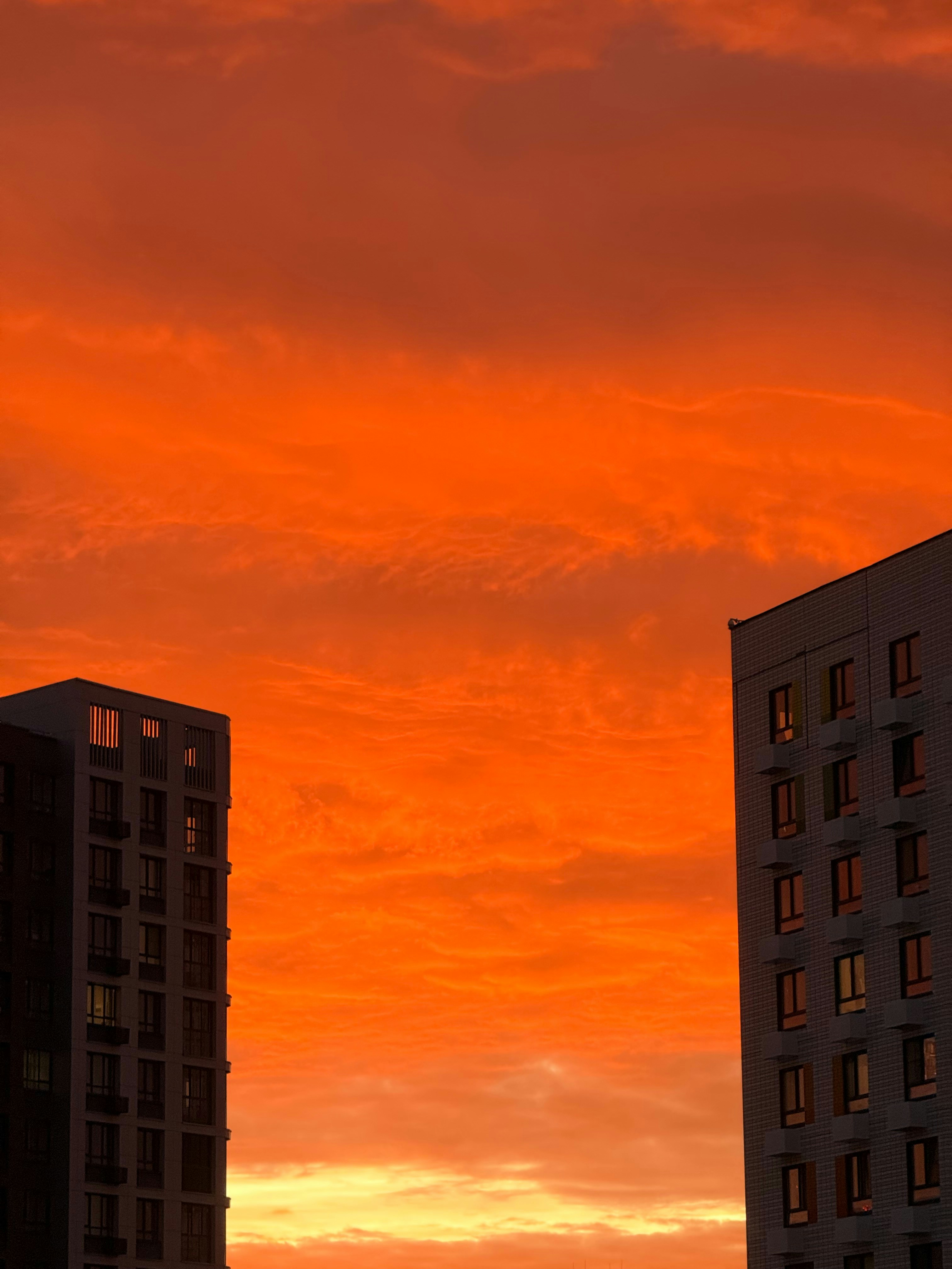 Two modern apartment buildings framing a vibrant orange sky at low sun
