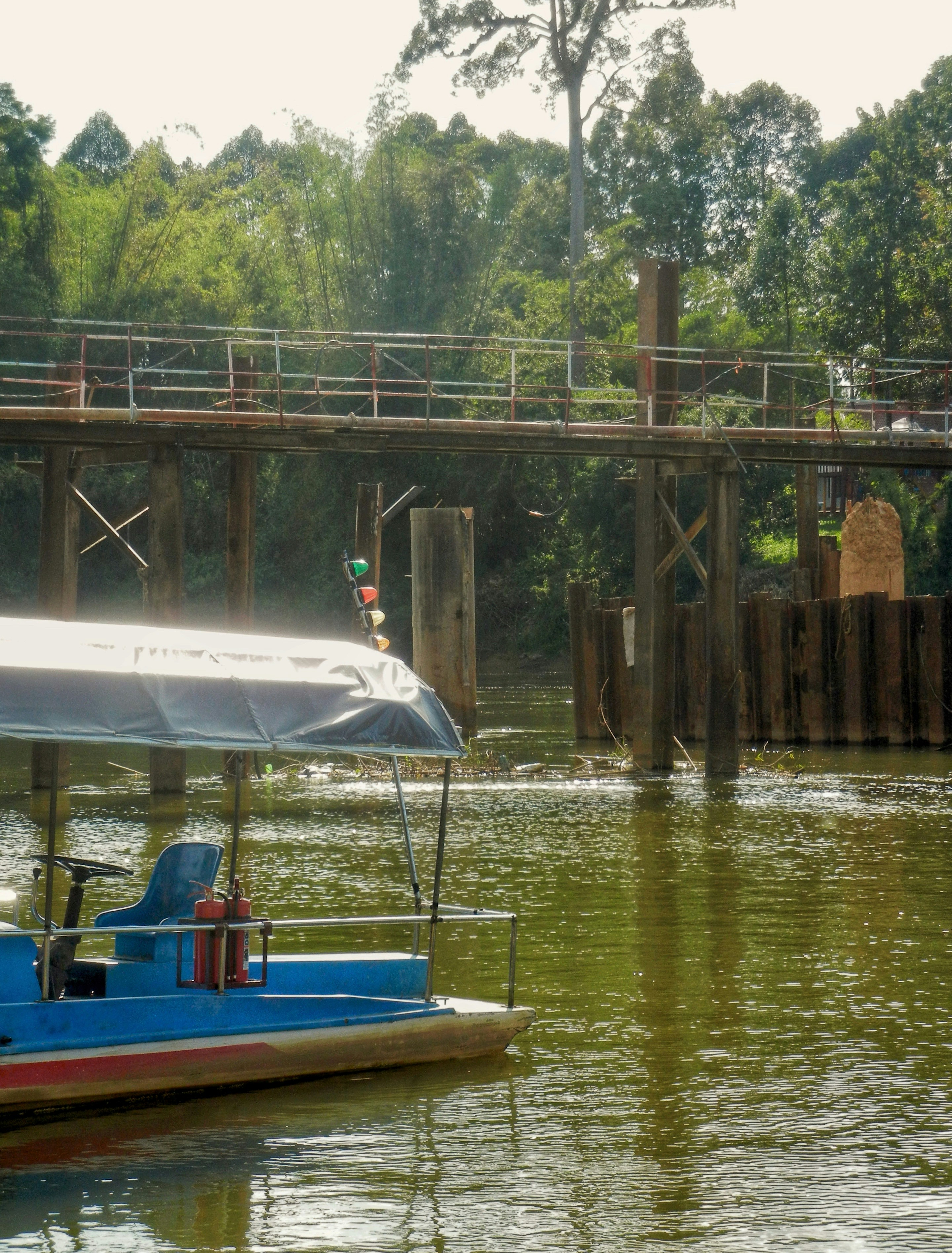 Sebuah perahu biru dengan kanopi yang berlabuh di dekat jembatan kayu di atas sungai