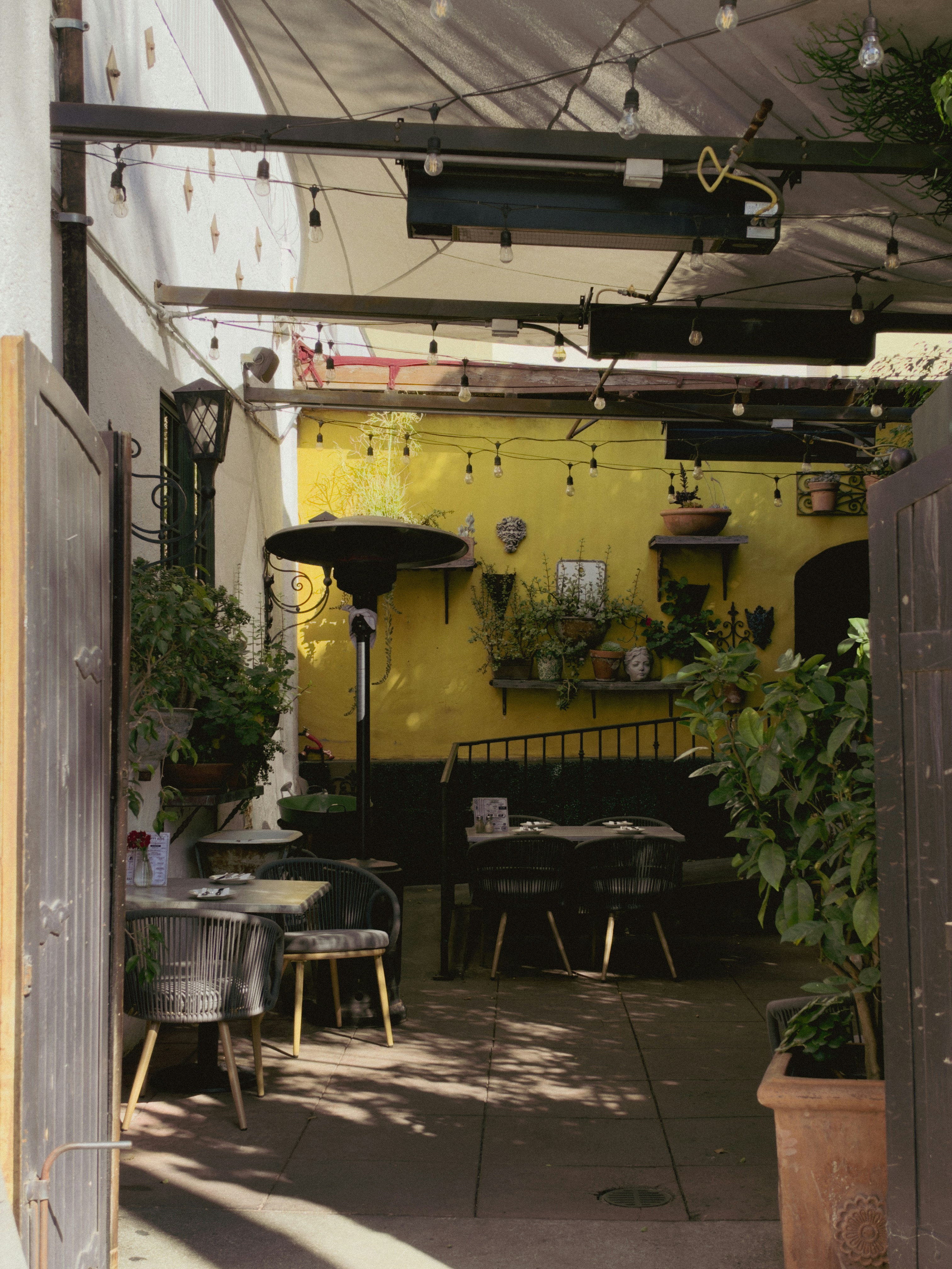 Un patio esterno di ristorante con tavoli e sedie contro una parete gialla brillante
