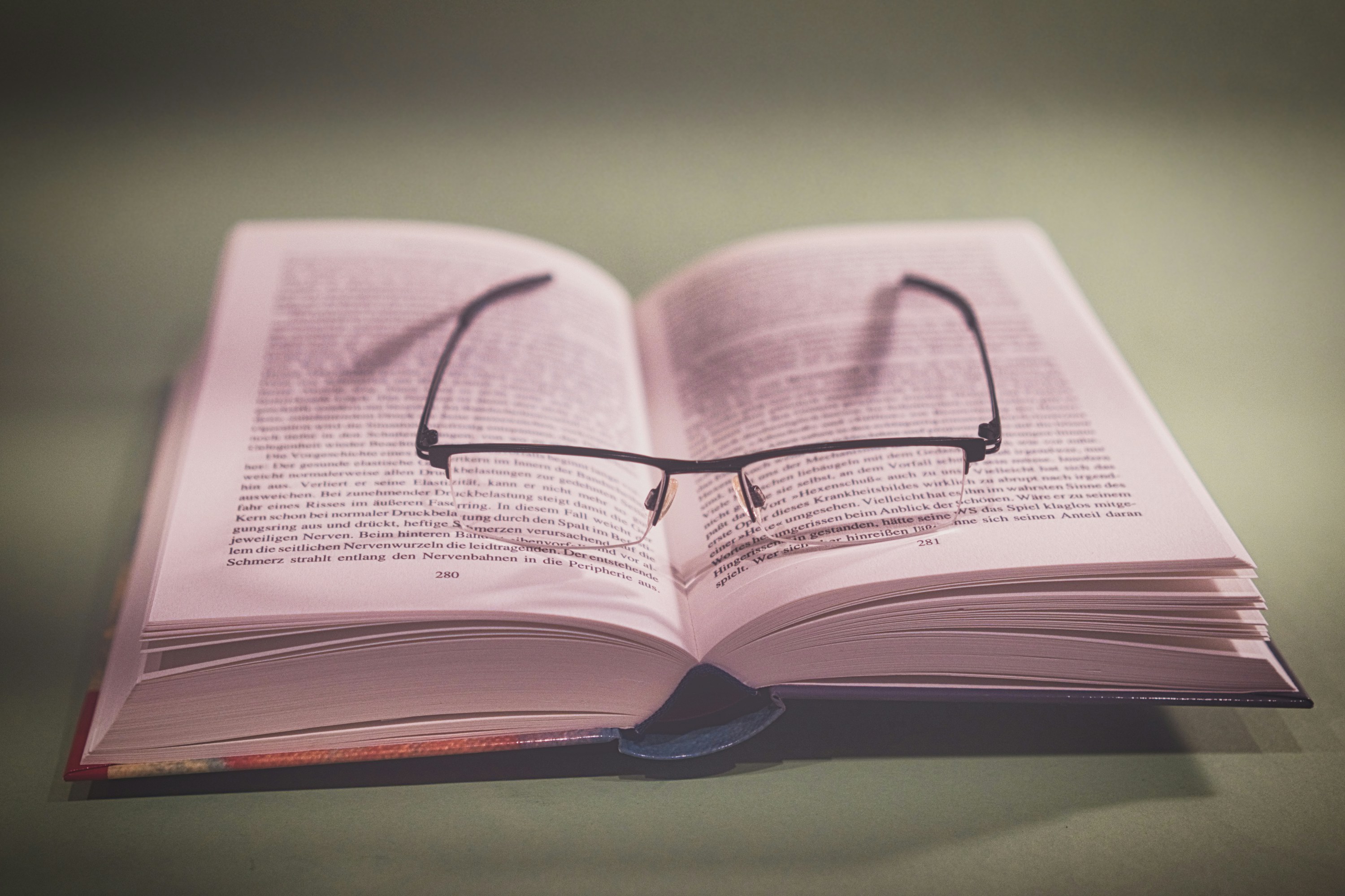 A pair of glasses resting on an open book with printed text