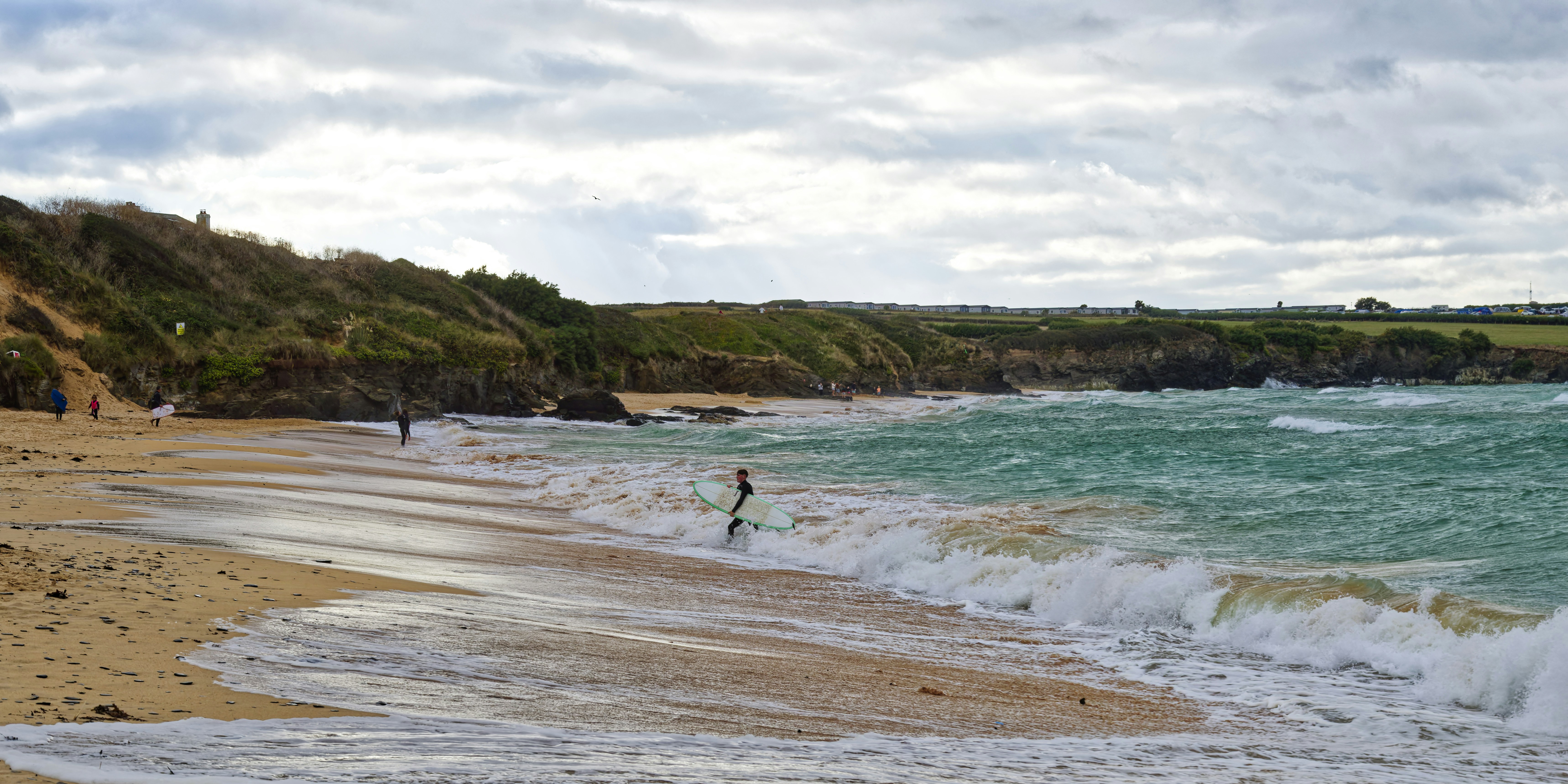 A surfer carrying a board into the turquoise waves on a sandy beach