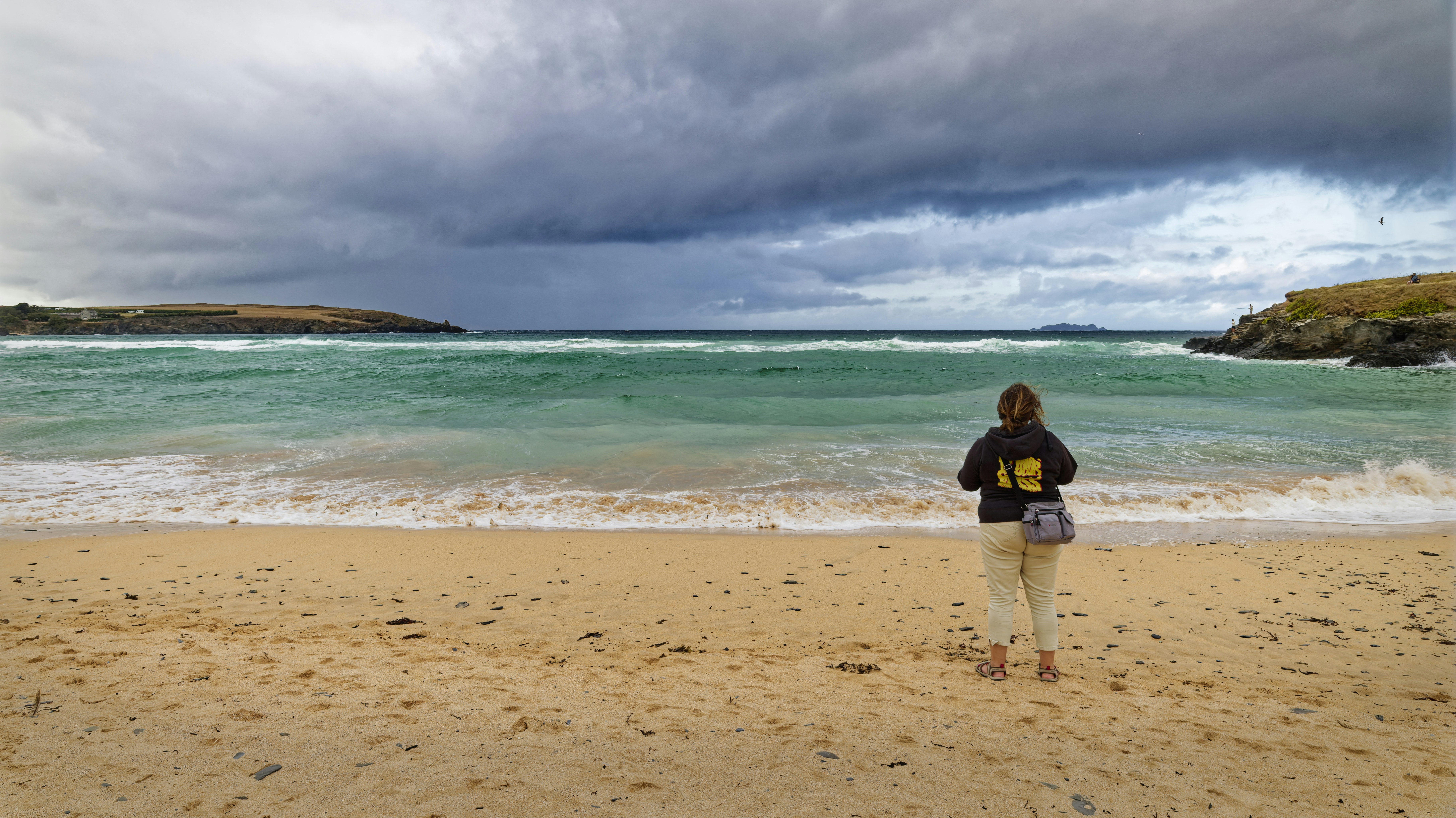 A person in a dark hoodie and light trousers on a sandy beach
