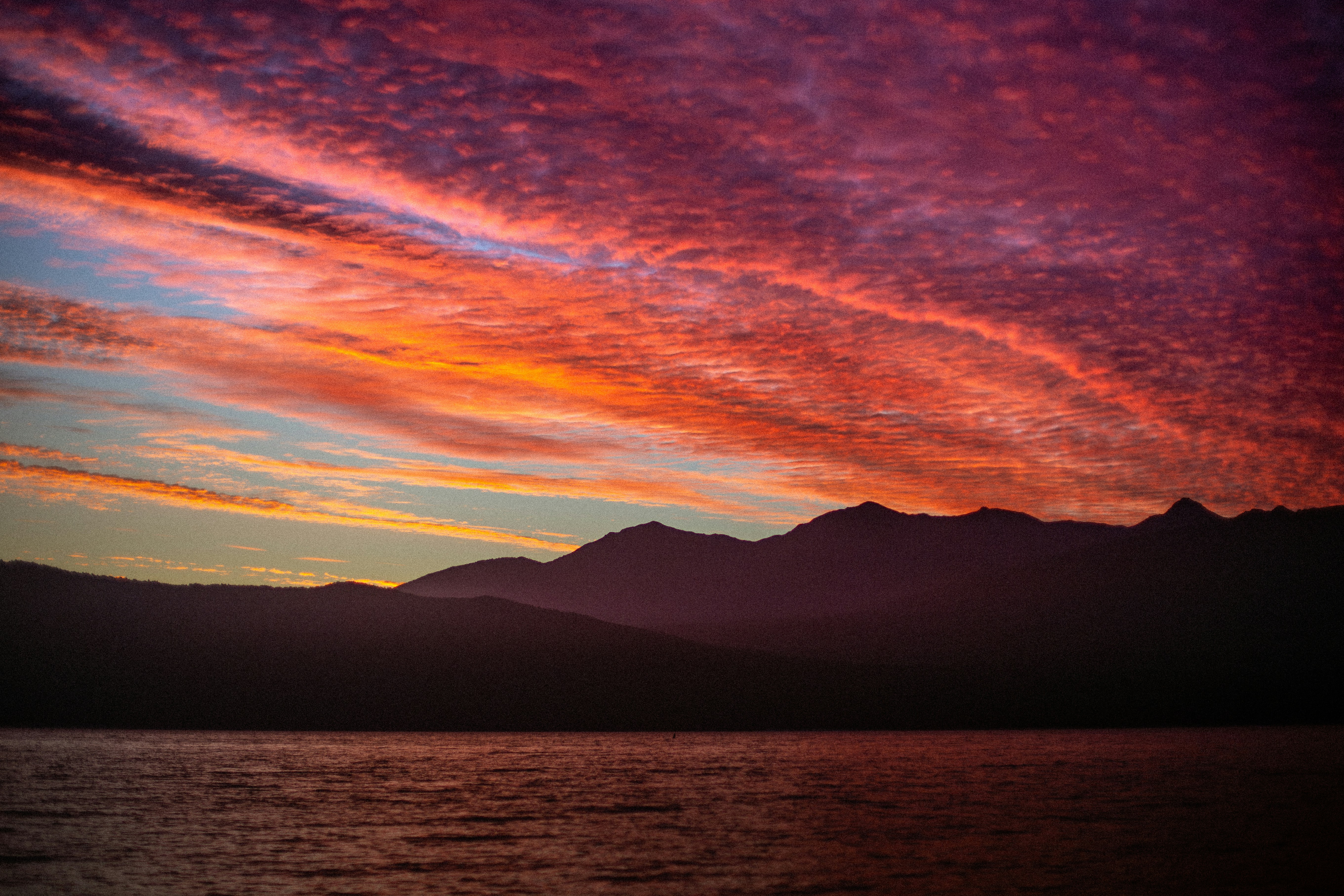 Silhouetted mountains against a vibrant orange and purple sky above dark water