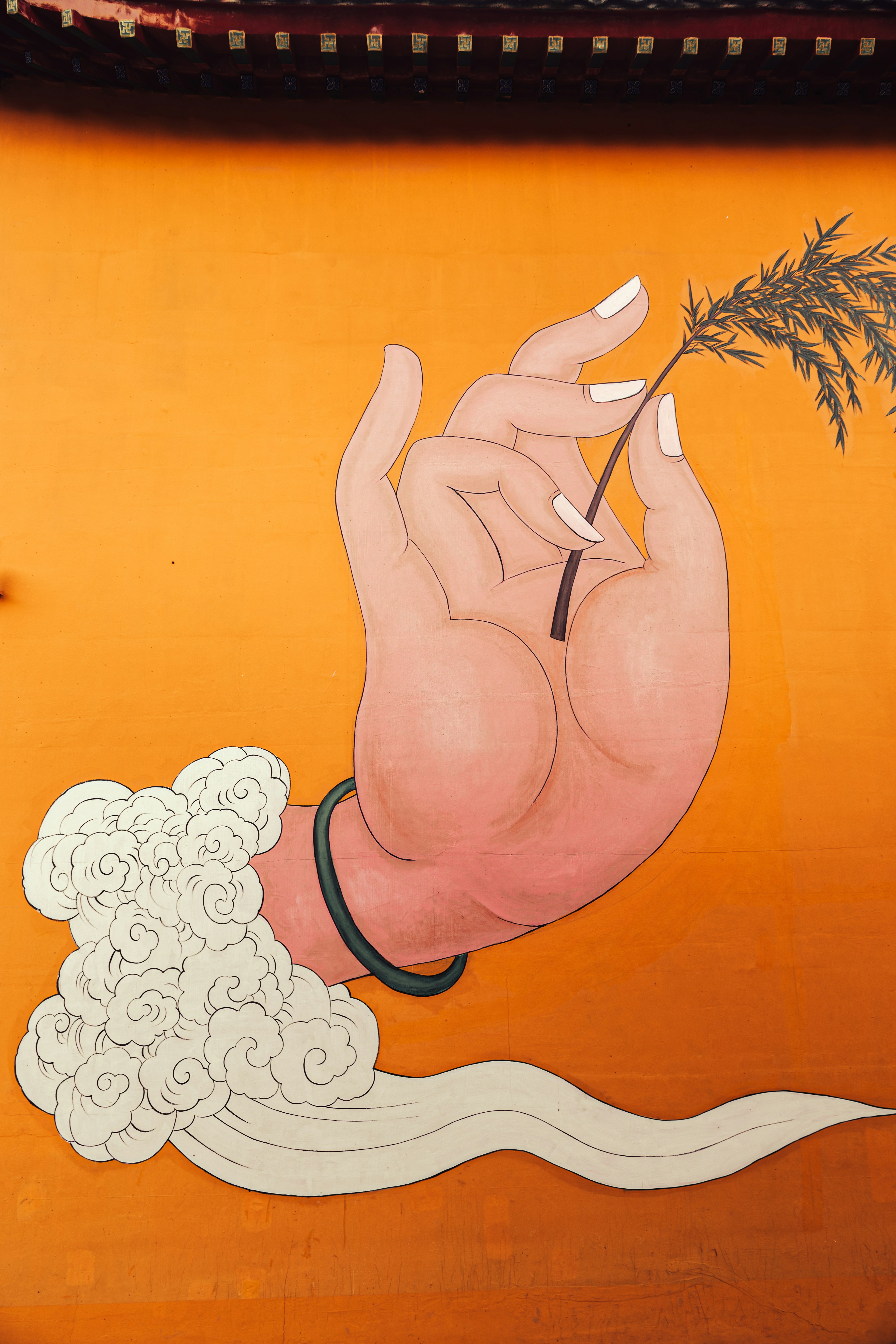 A painted hand holding a small branch against a vibrant orange wall