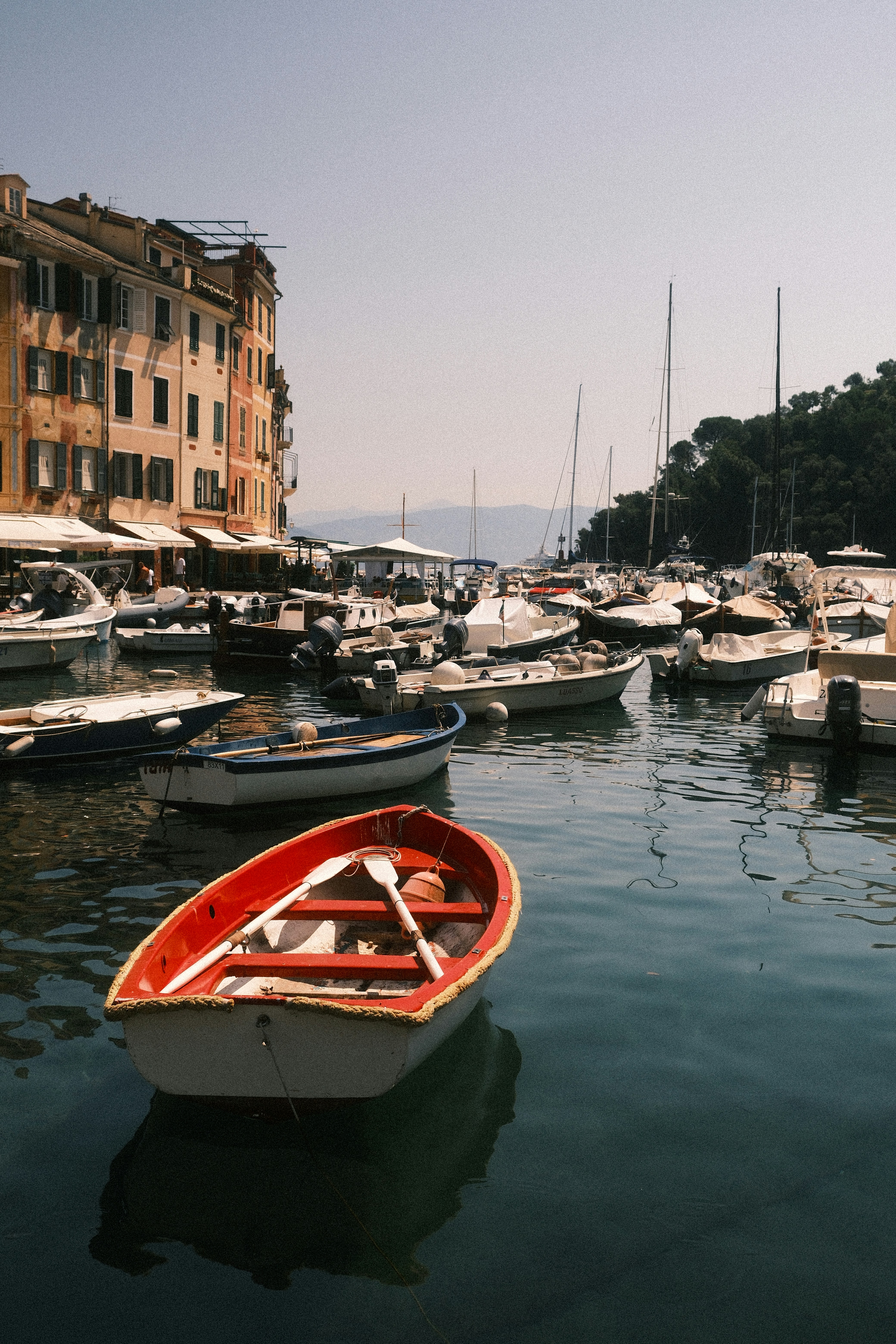 A red rowboat in a harbor filled with small boats near colorful buildings
