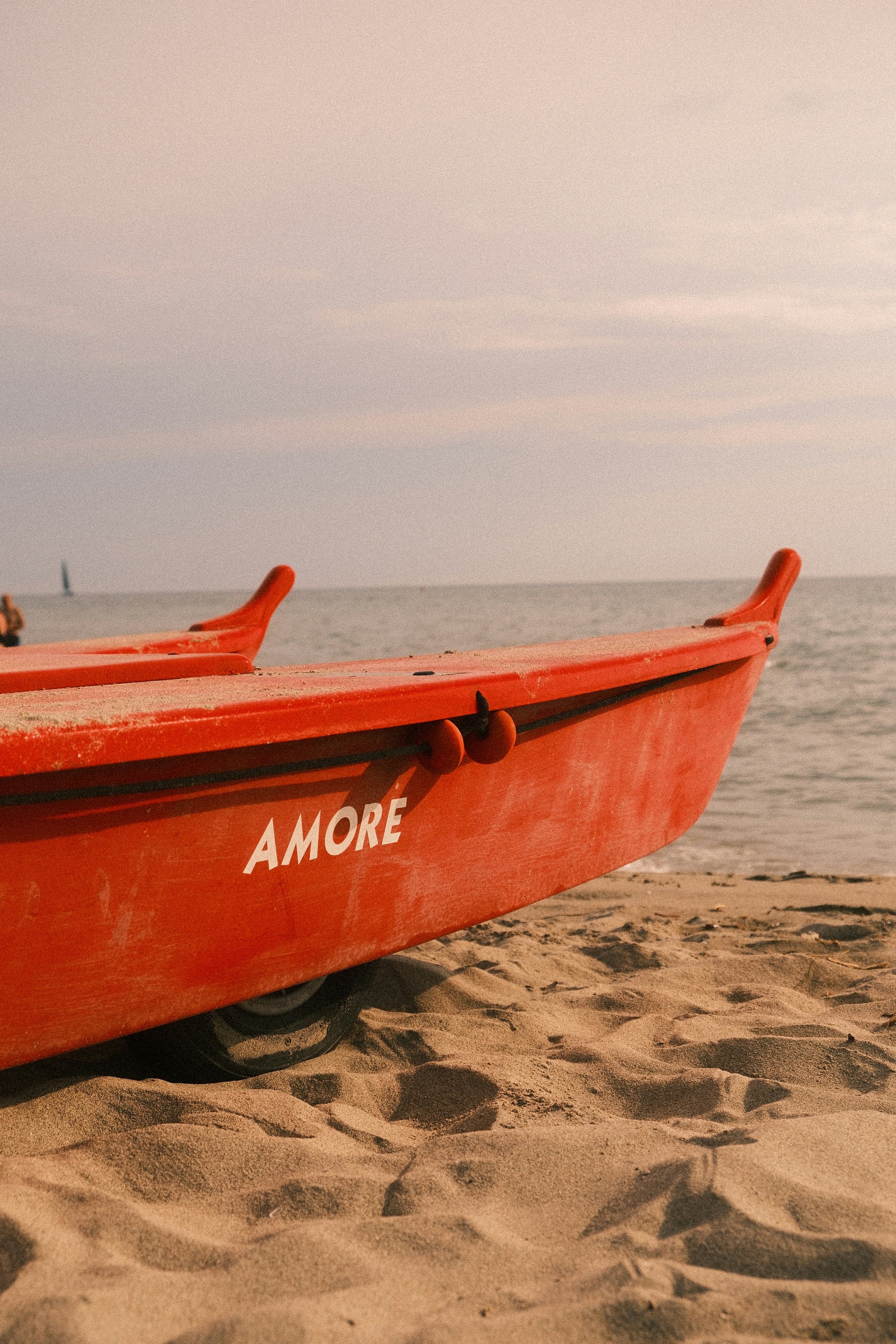 A red lifeguard boat with the word AMORE on the side on a sandy beach