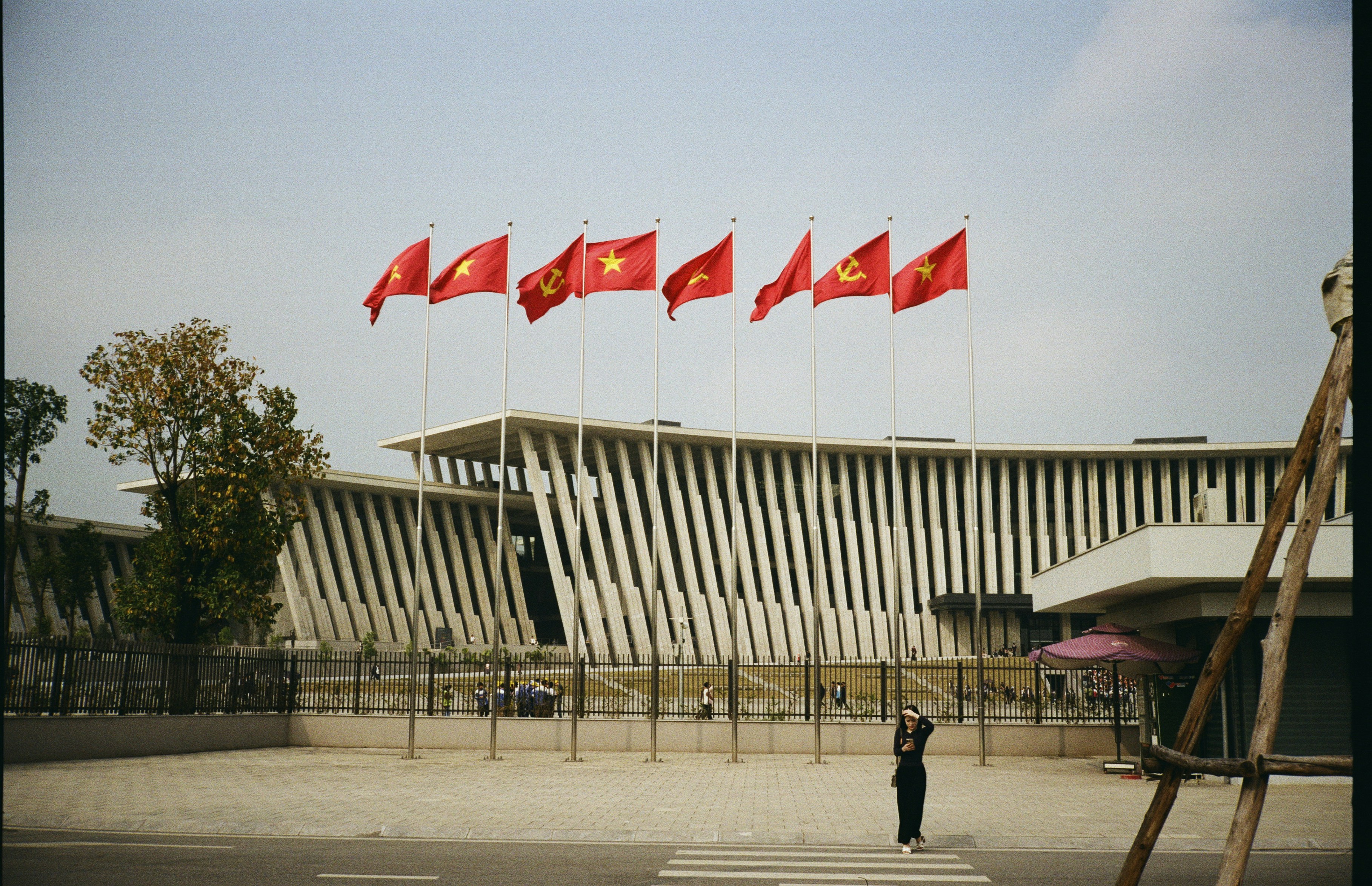 Red flags flying in front of a modern building with concrete pillars in Hanoi