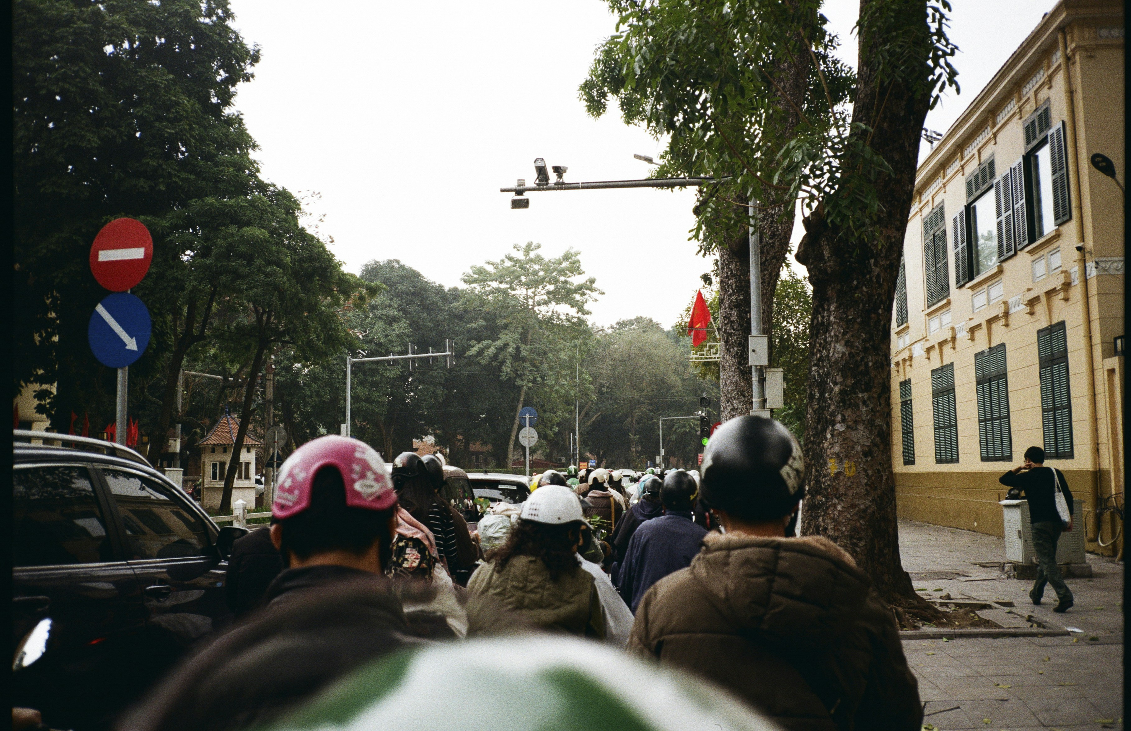 Motorcyclists in helmets riding on a city street past a yellow colonial building
