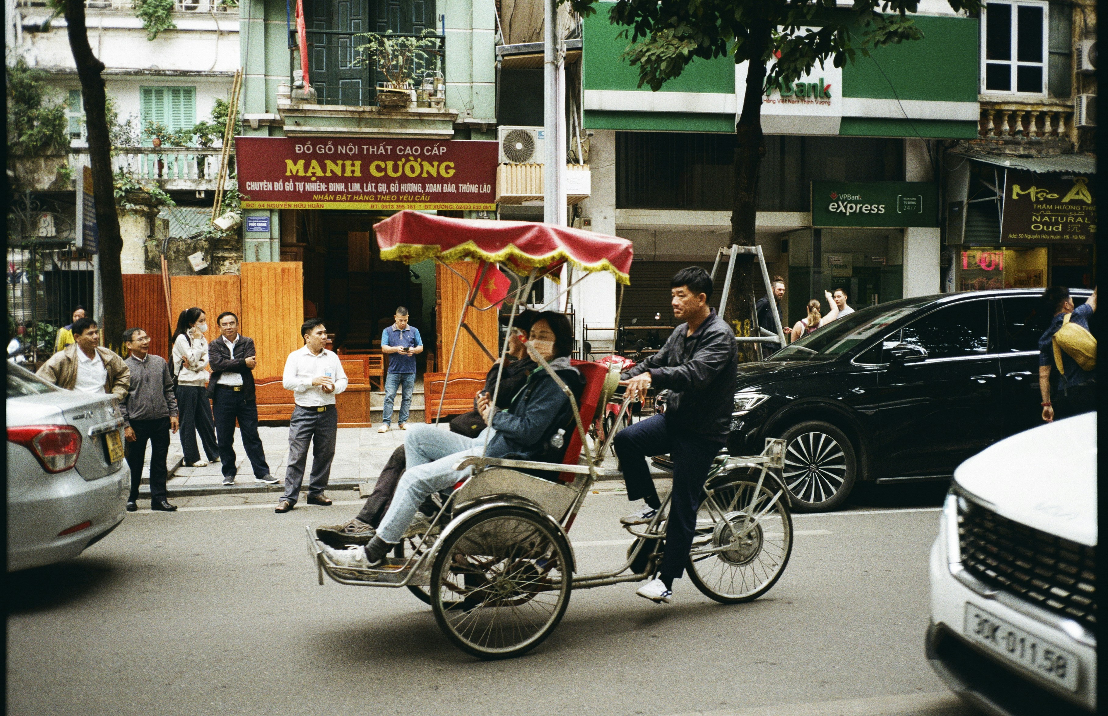 A man pedaling a cyclo with a passenger on a busy street in Hanoi
