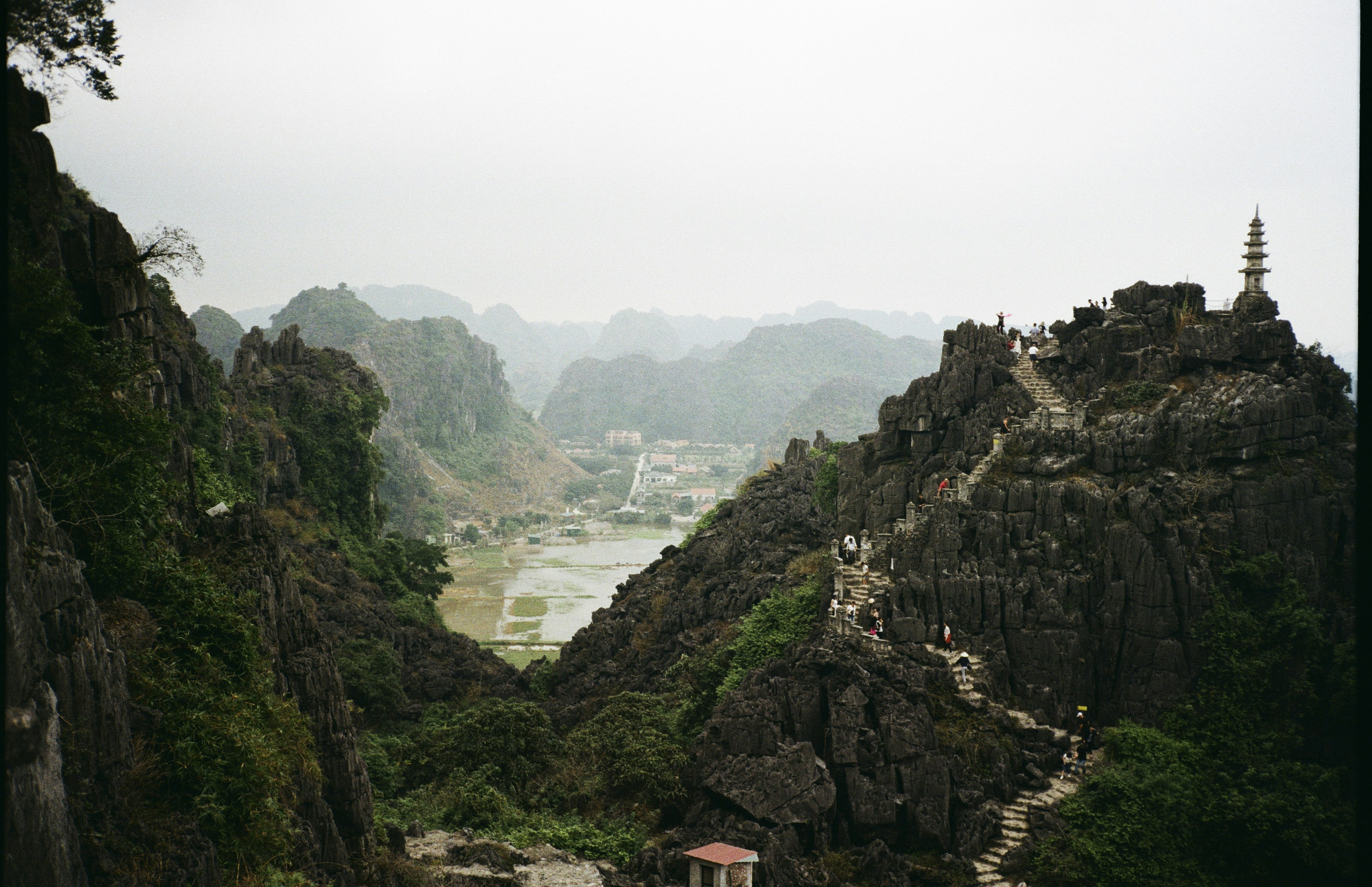 People climbing stone stairs on a rocky mountain peak with a pagoda in Ninh Binh