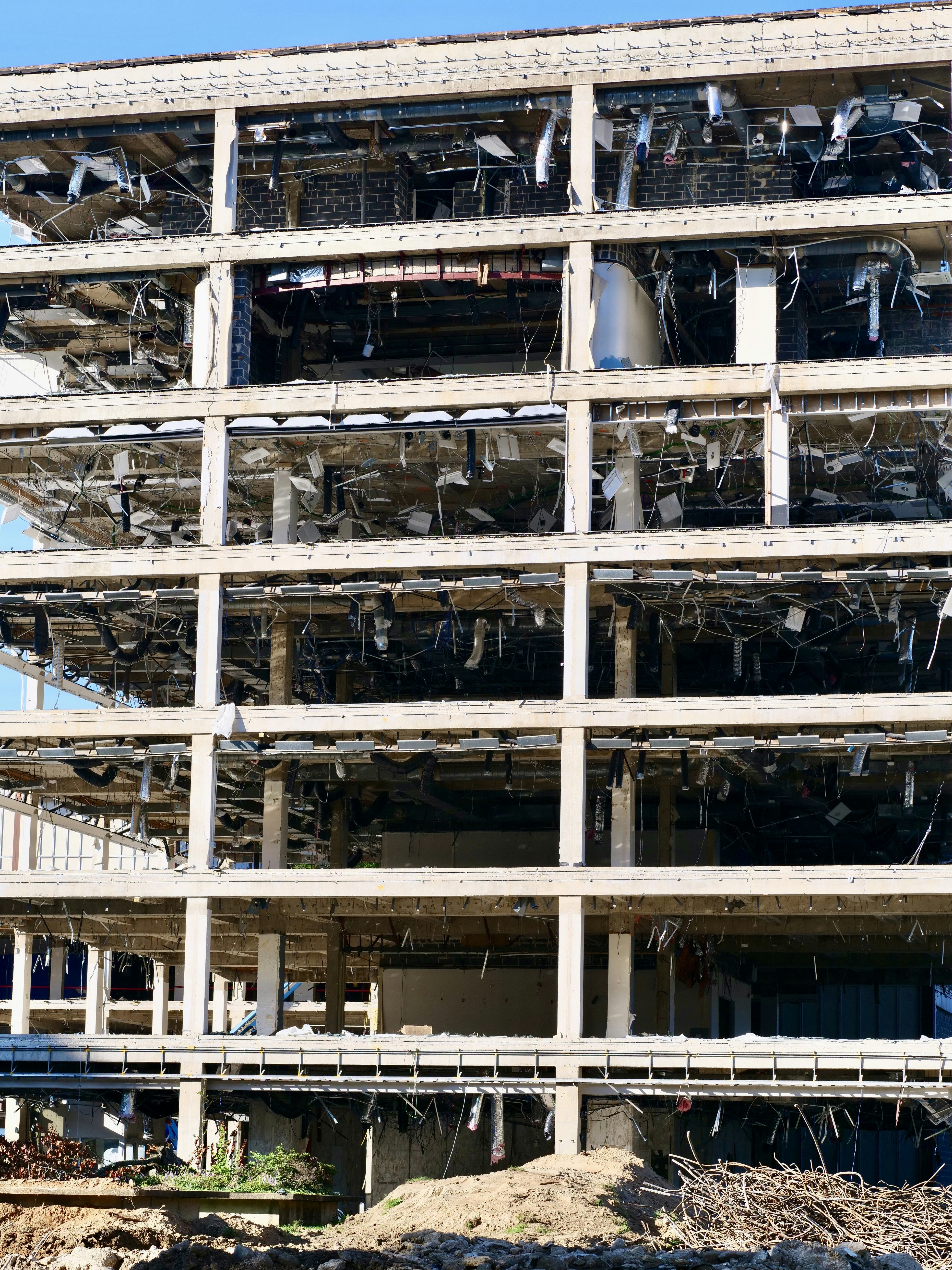 A multi-story building under demolition with exposed concrete beams and hanging debris