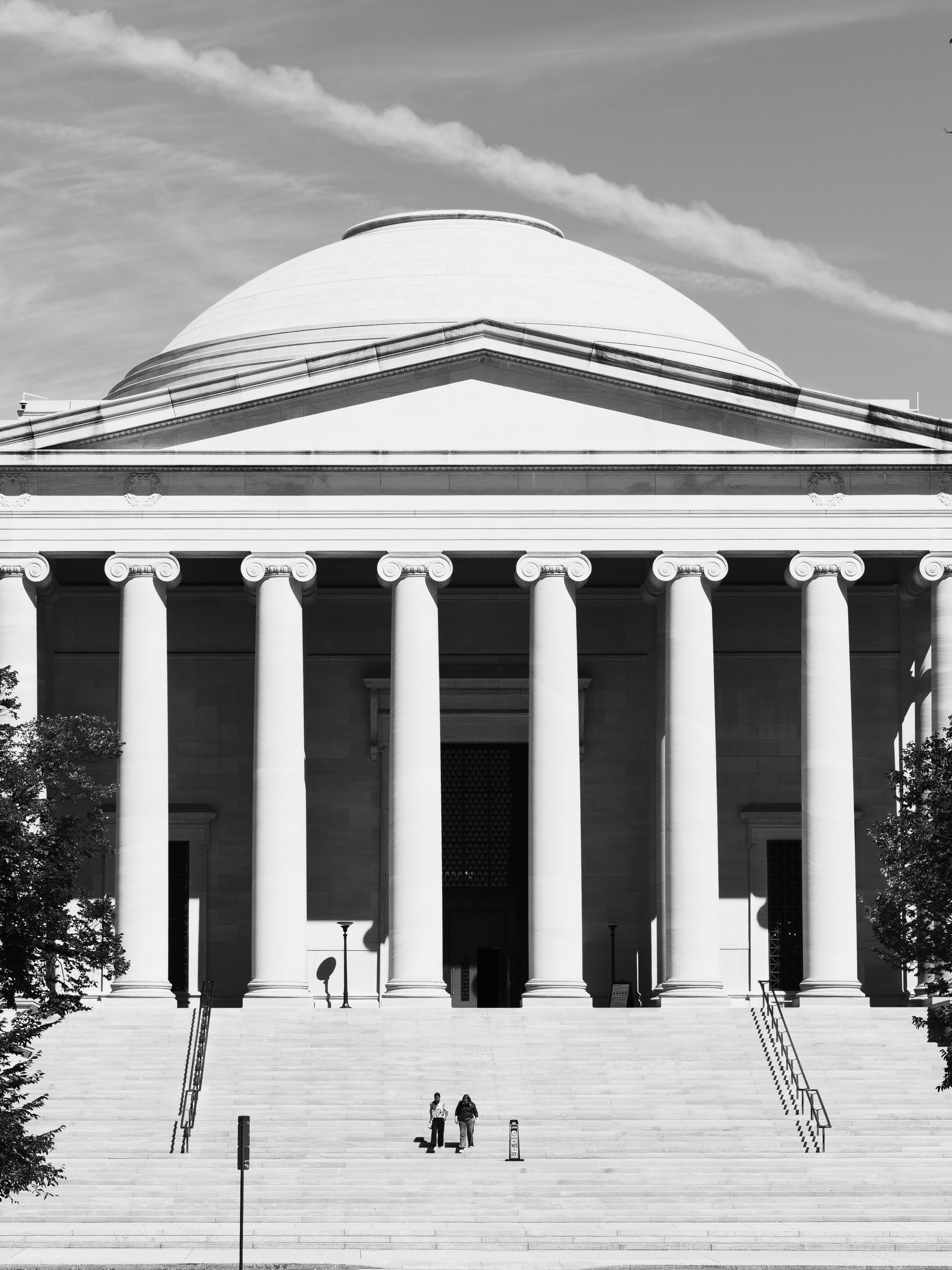 Two people walking up the wide stone steps of a neoclassical building with columns