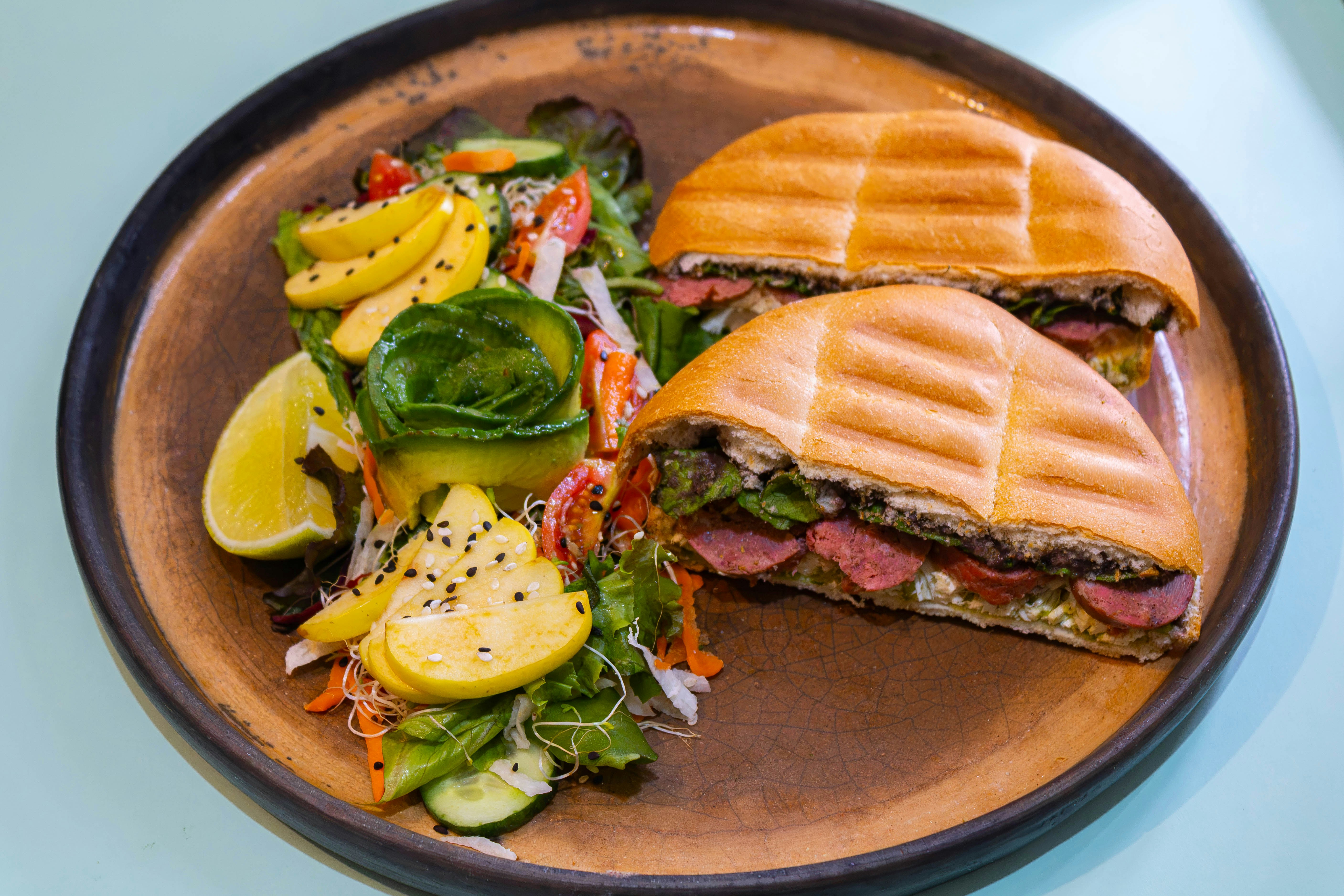 A halved panini sandwich beside a fresh salad with apple slices on a plate