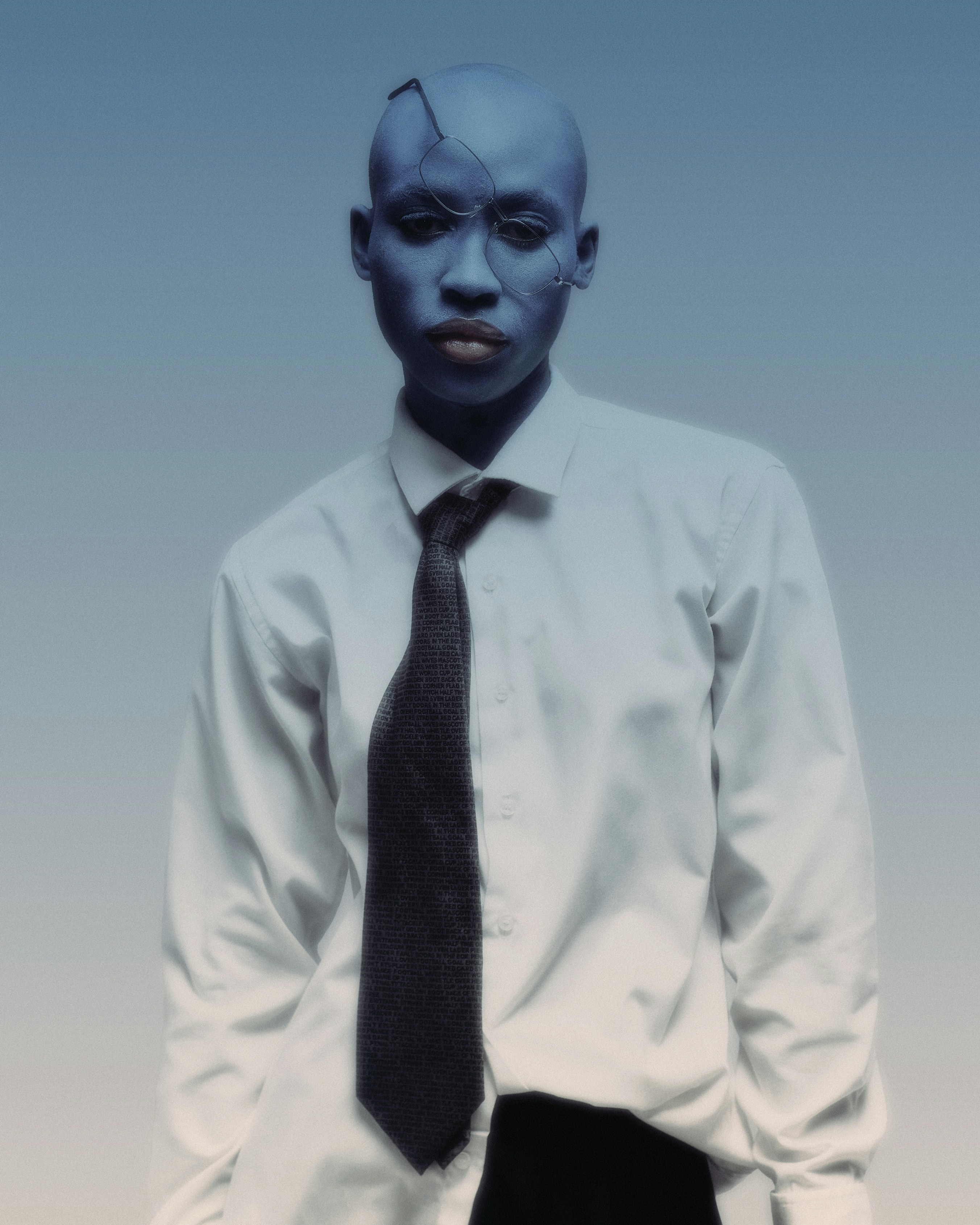 A person with a shaved head wearing a white shirt and dark tie