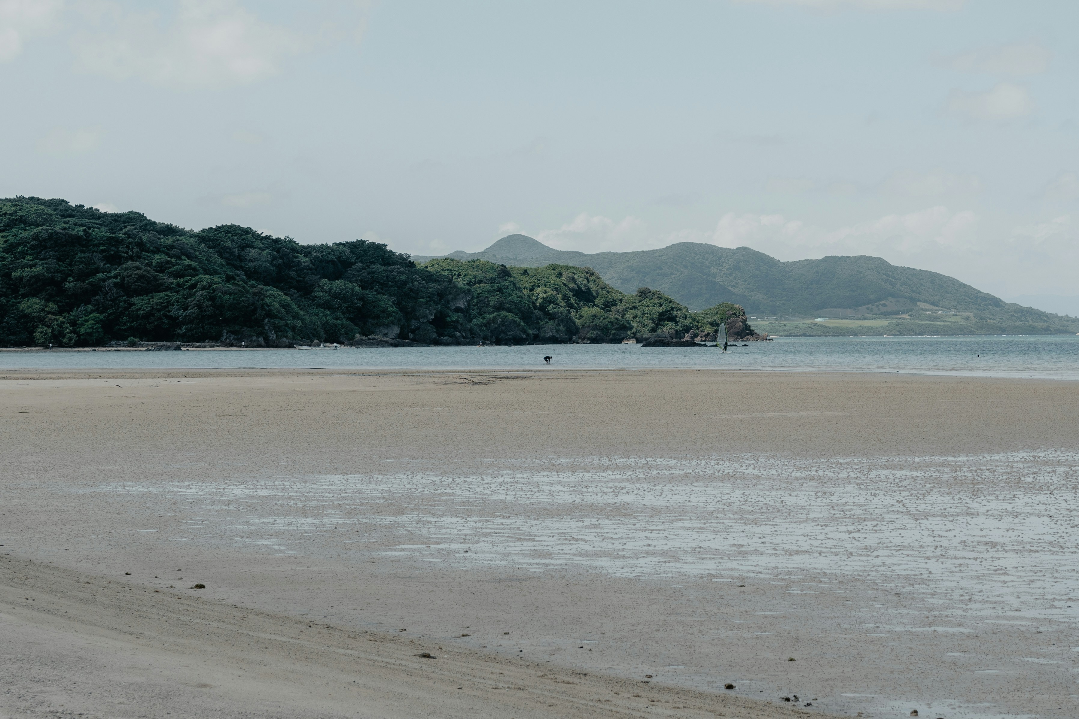 Ein breiter Sandstrand bei Ebbe mit entfernten grünen Hügeln und Bergen