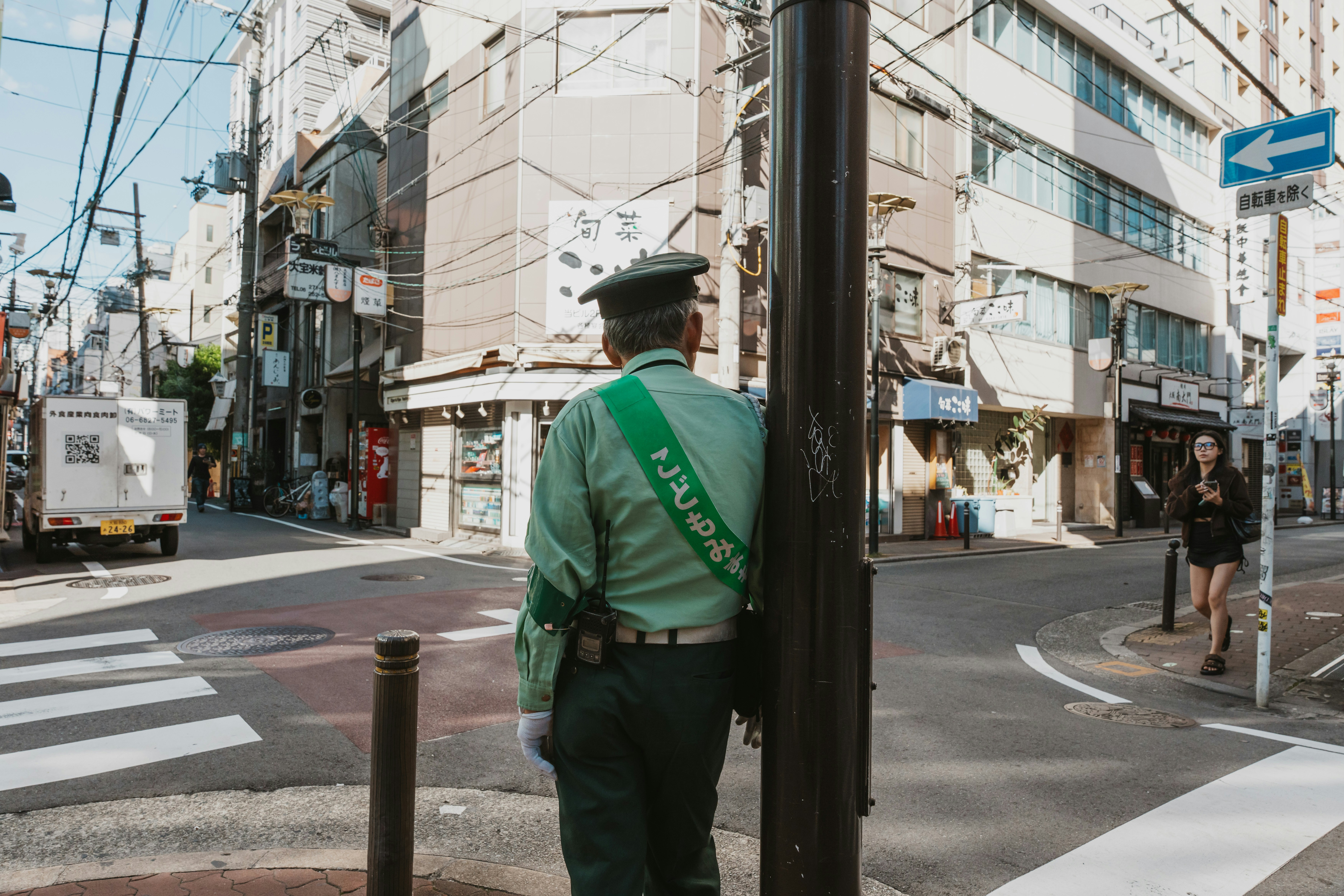 A traffic guard in a green uniform at a sunny street intersection