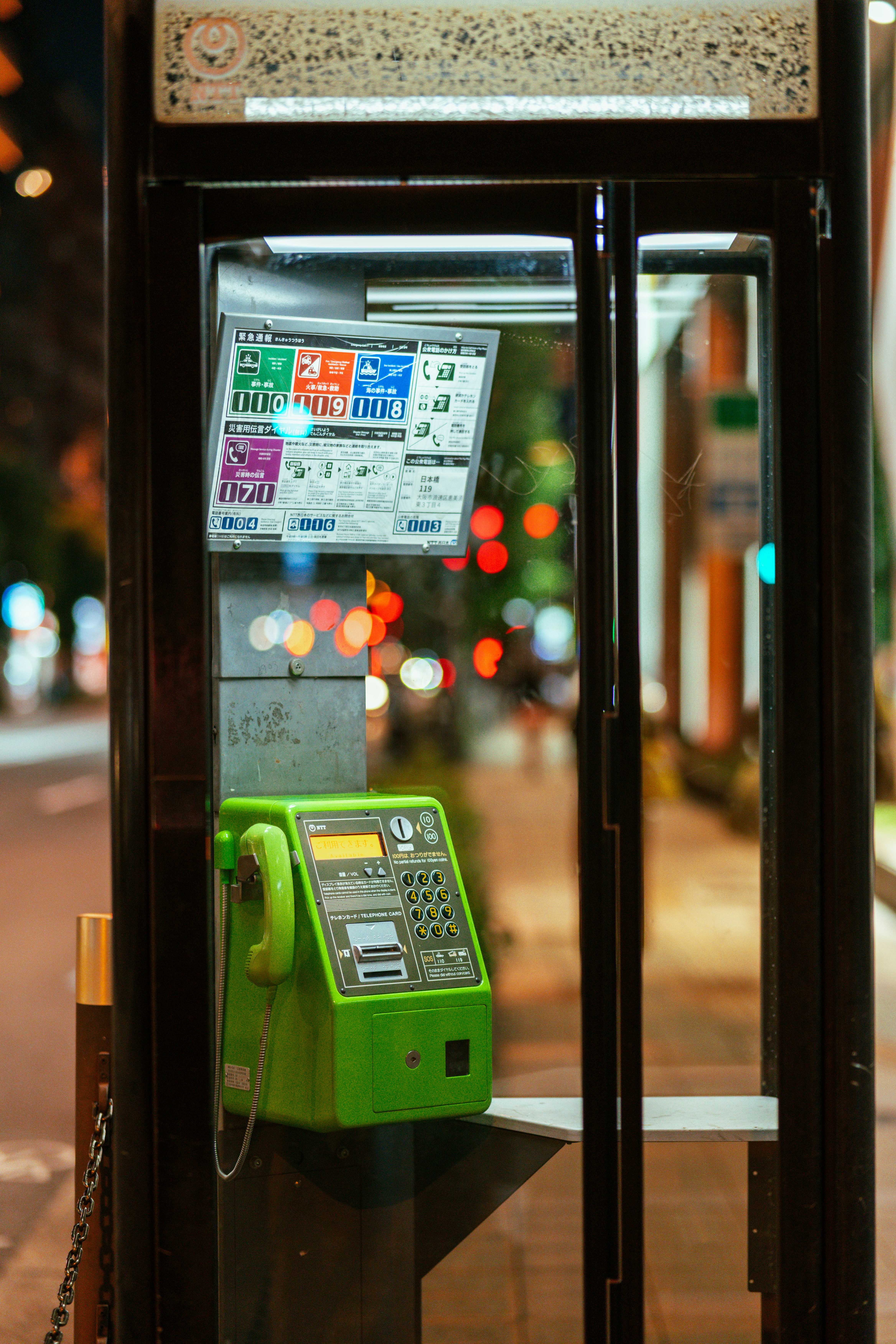 Un telefono pubblico verde all'interno di una cabina di vetro in una strada cittadina di notte