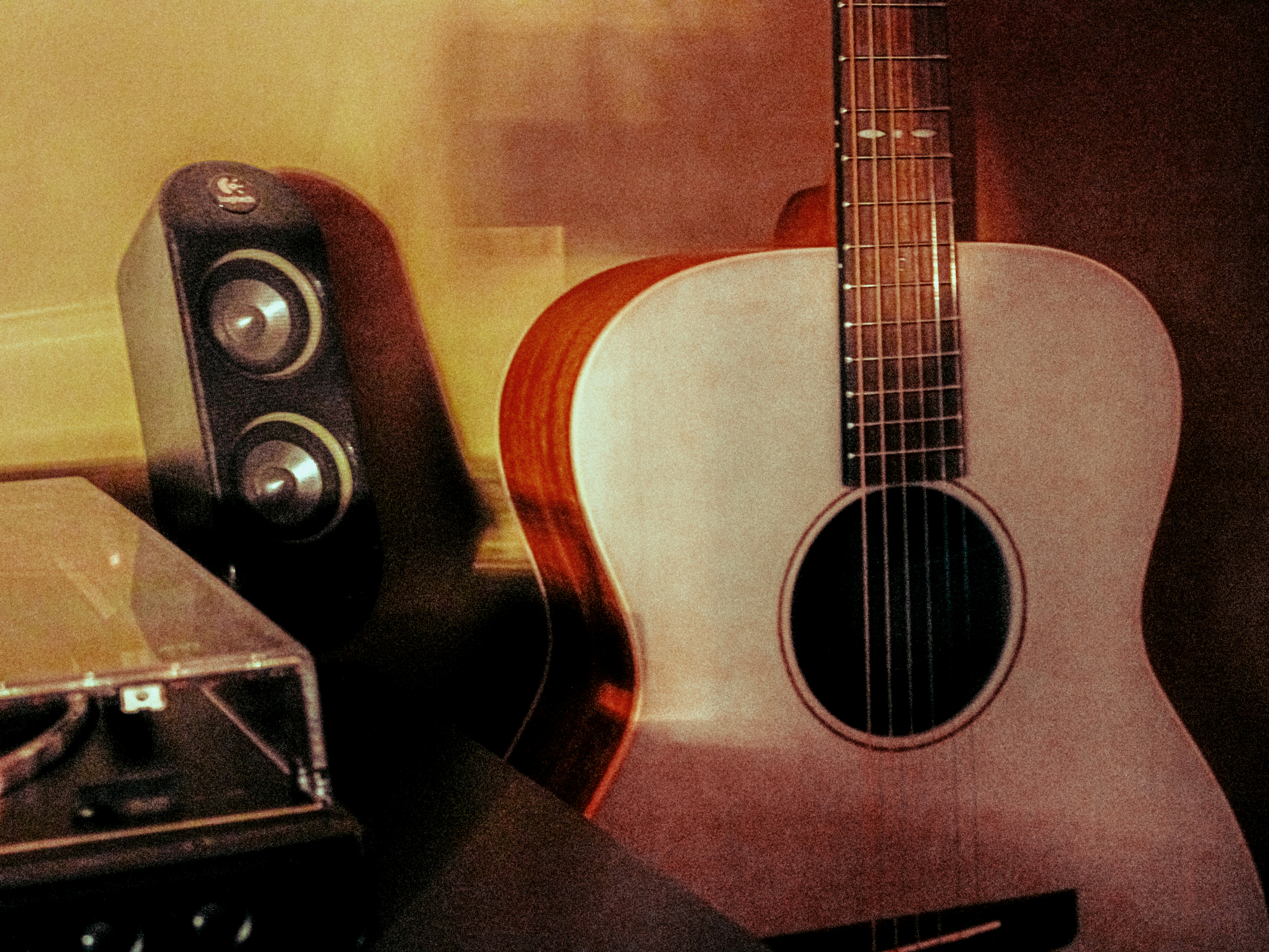 An acoustic guitar beside a speaker and a turntable in warm light