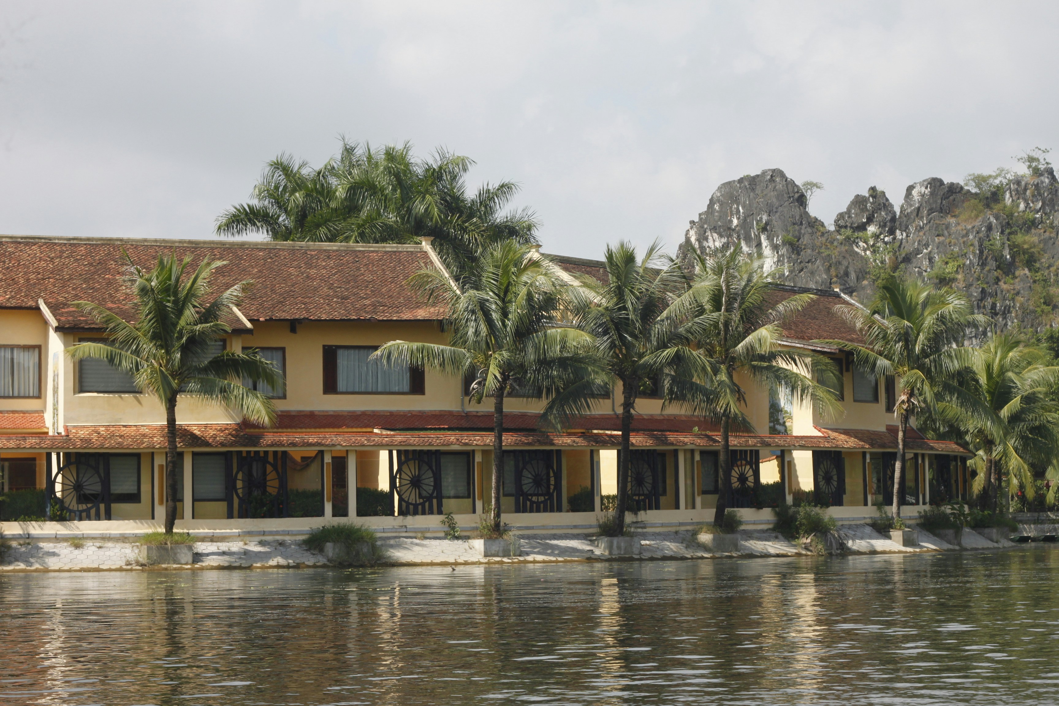 A yellow building with a tiled roof beside a river with palm trees