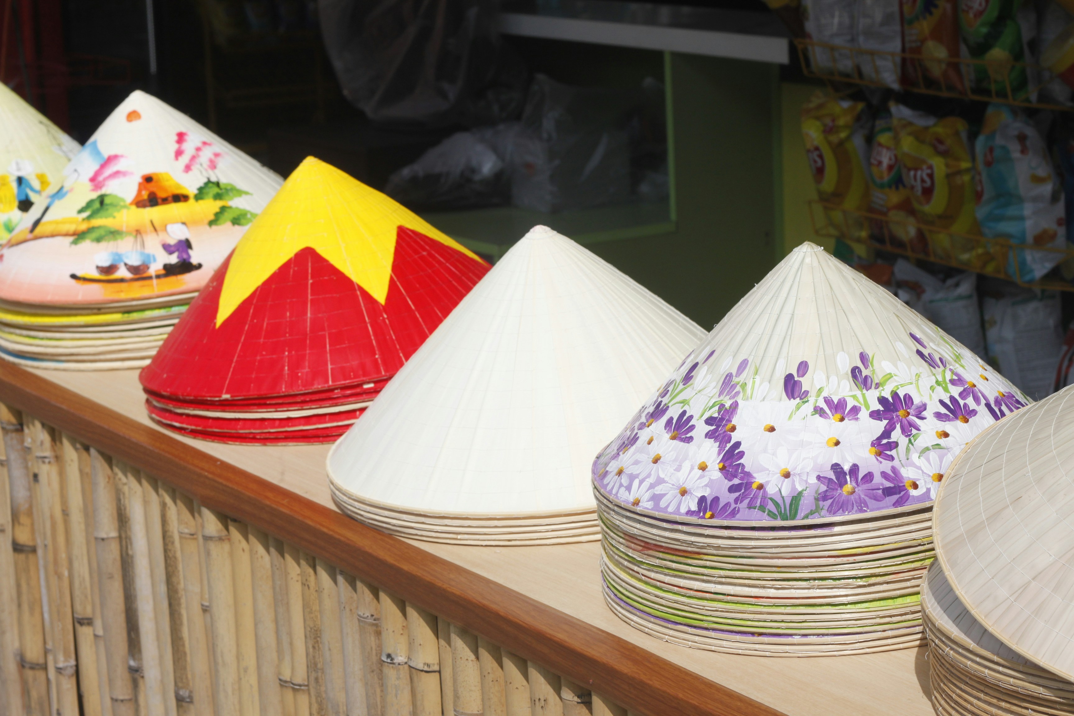 Stacks of conical hats with painted floral designs on a bamboo counter