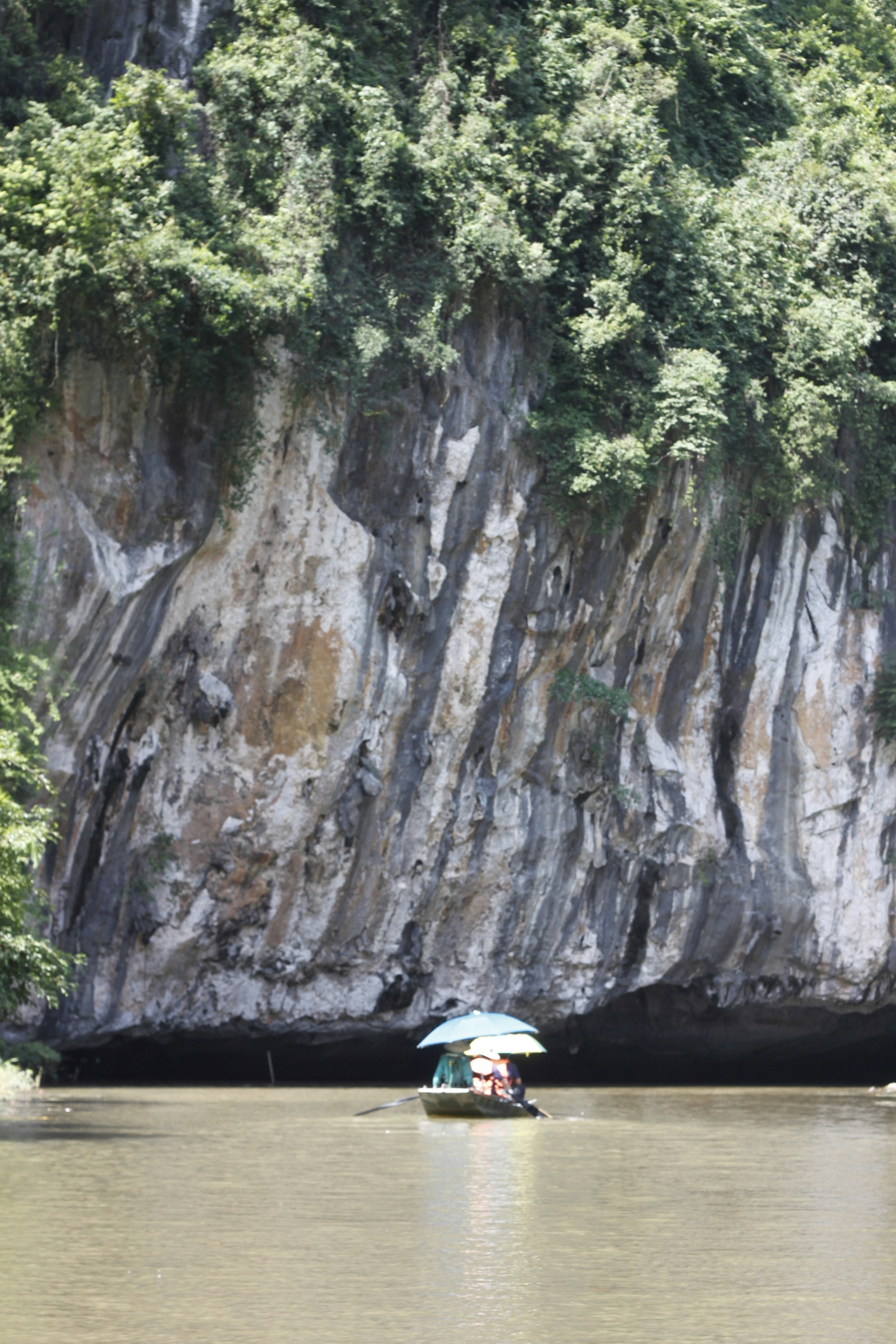 A small boat with a blue umbrella on a river beneath a limestone cliff