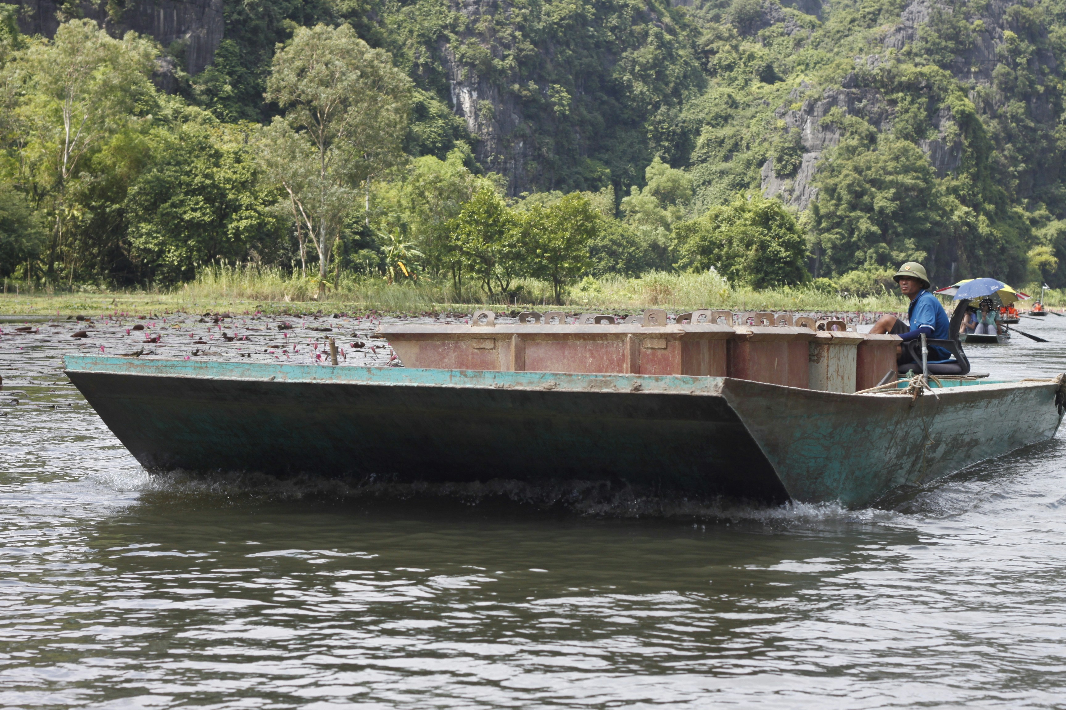 A person in a blue shirt steering a flat metal boat on a river