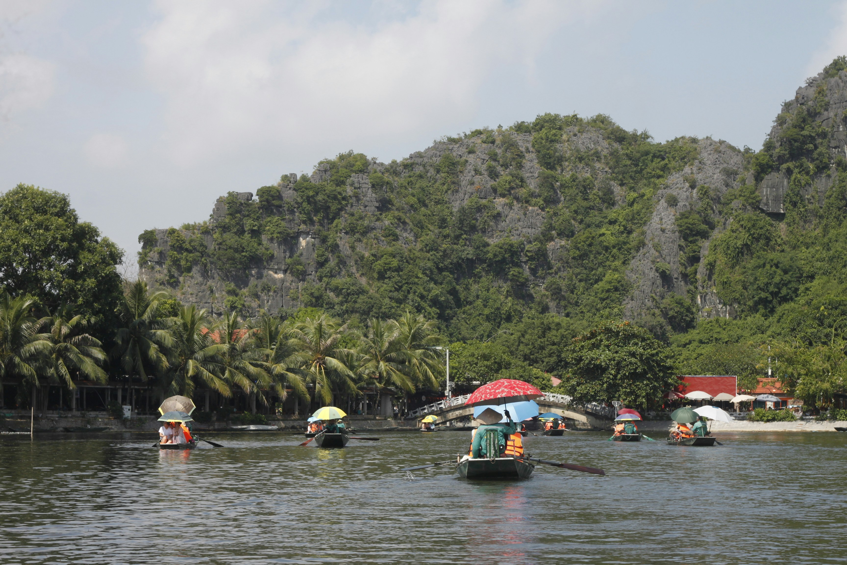 People in small boats with umbrellas on a river near limestone mountains