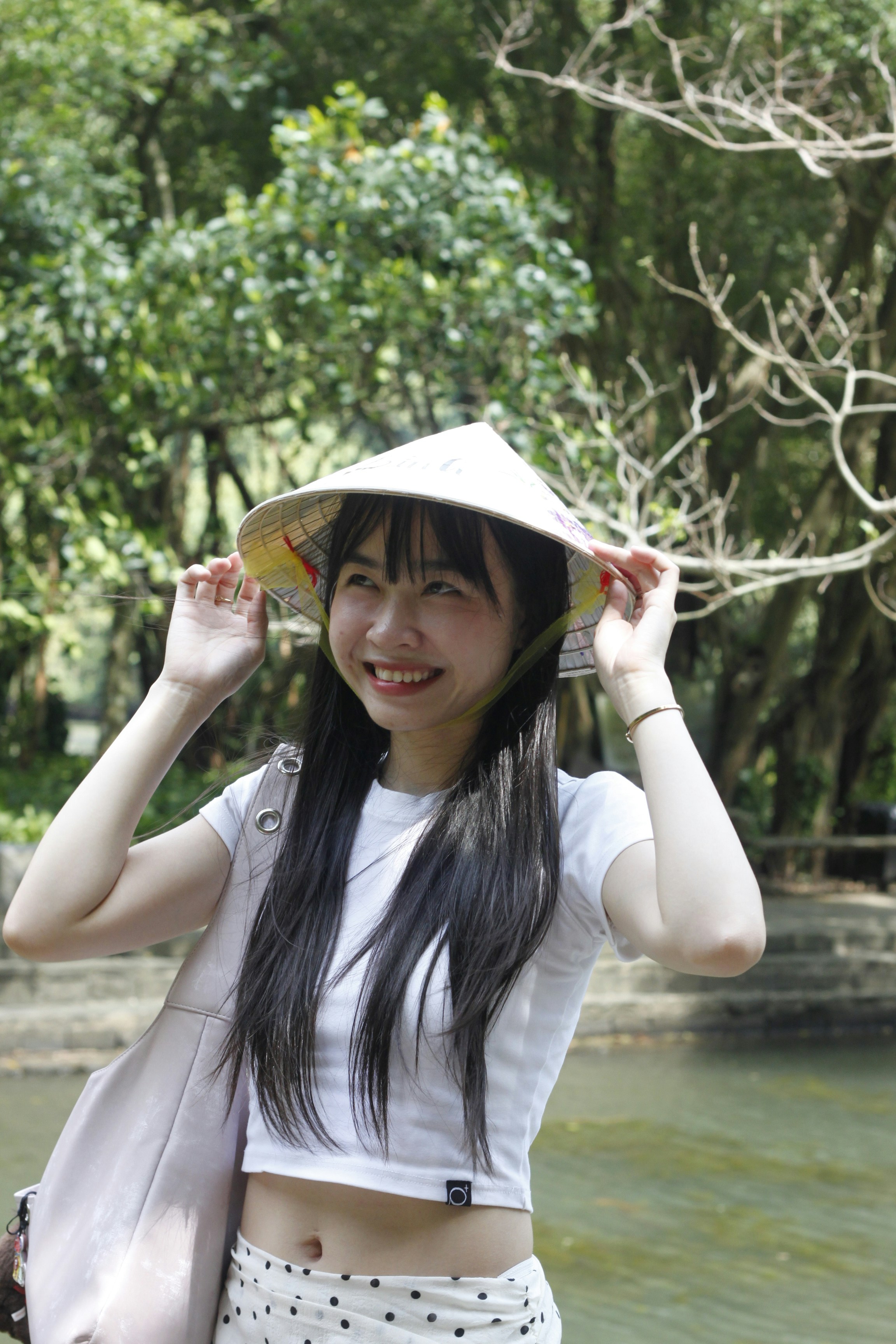A smiling woman wearing a conical hat in a lush green park