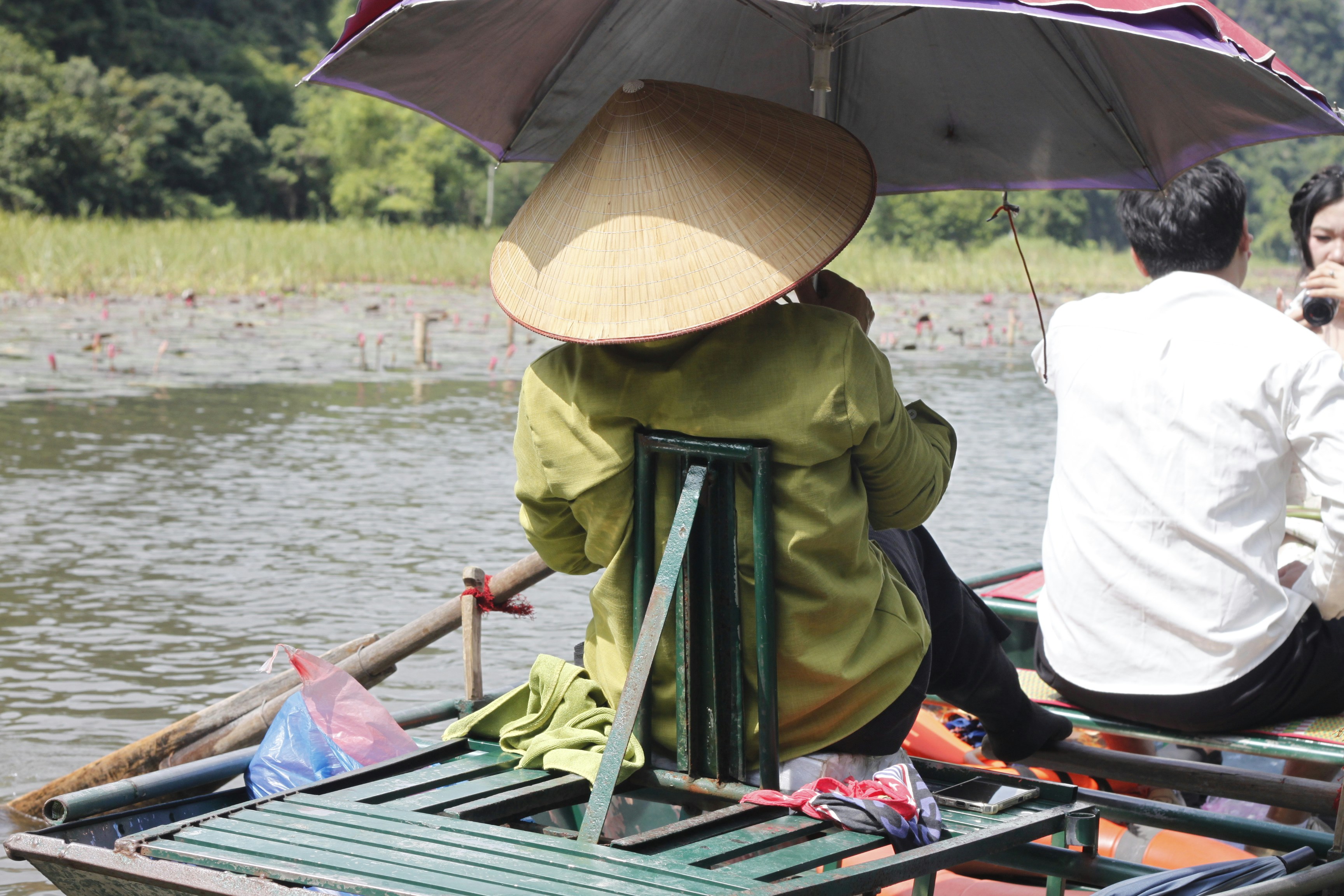 A person in a conical hat under an umbrella on a small boat
