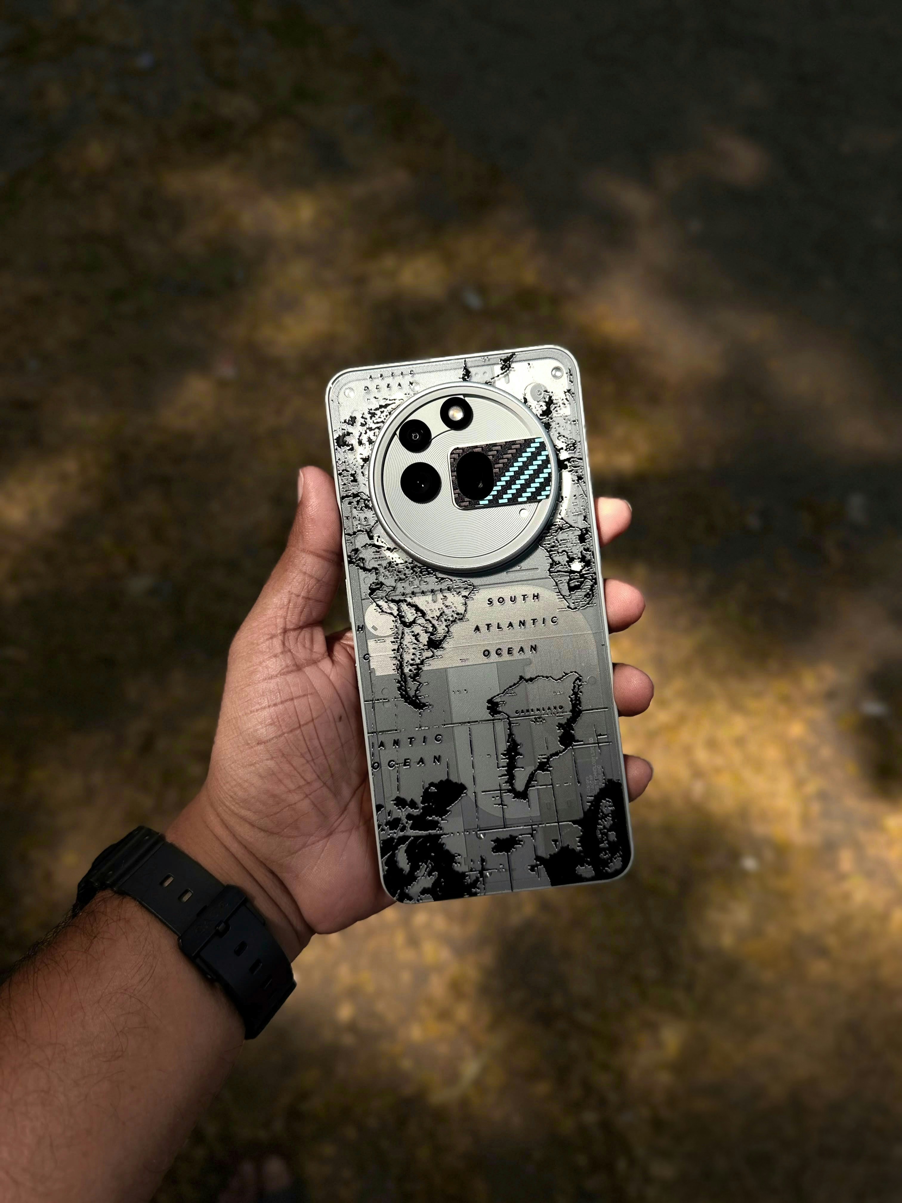 A hand holding a smartphone with a world map design on the back