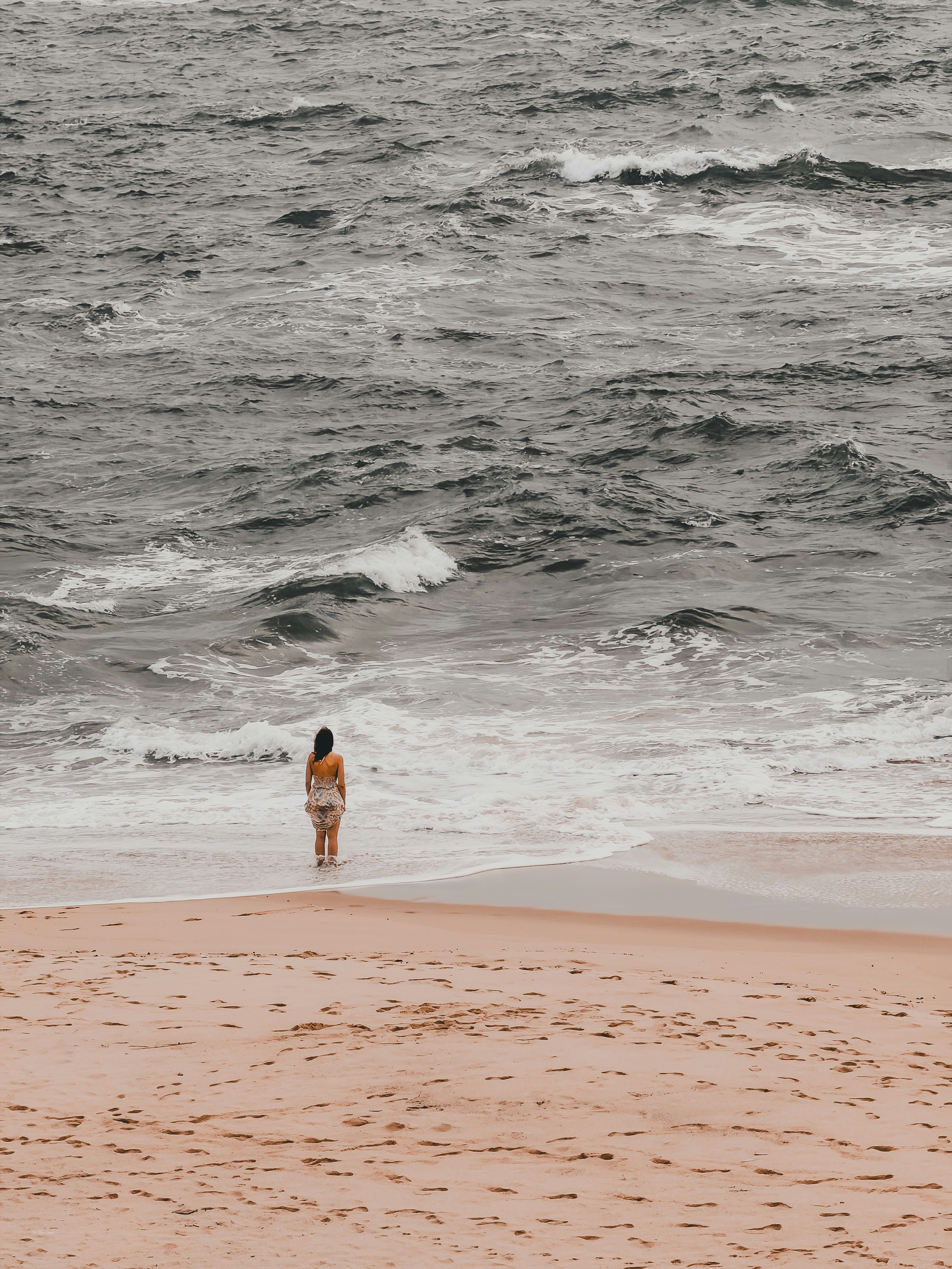 A woman in a patterned dress on a sandy beach facing the ocean