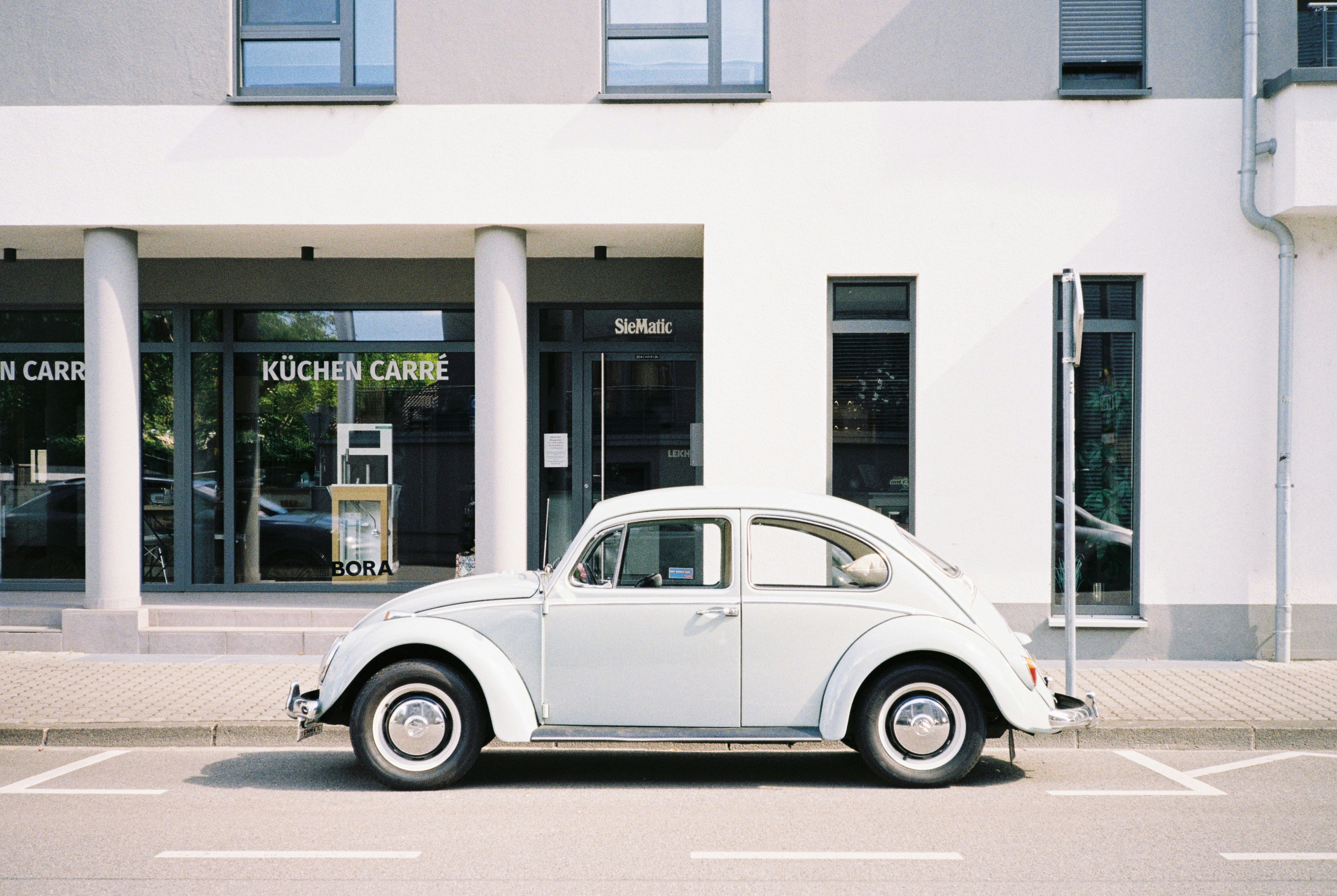 A light grey vintage Volkswagen Beetle parked on a street in front of a building