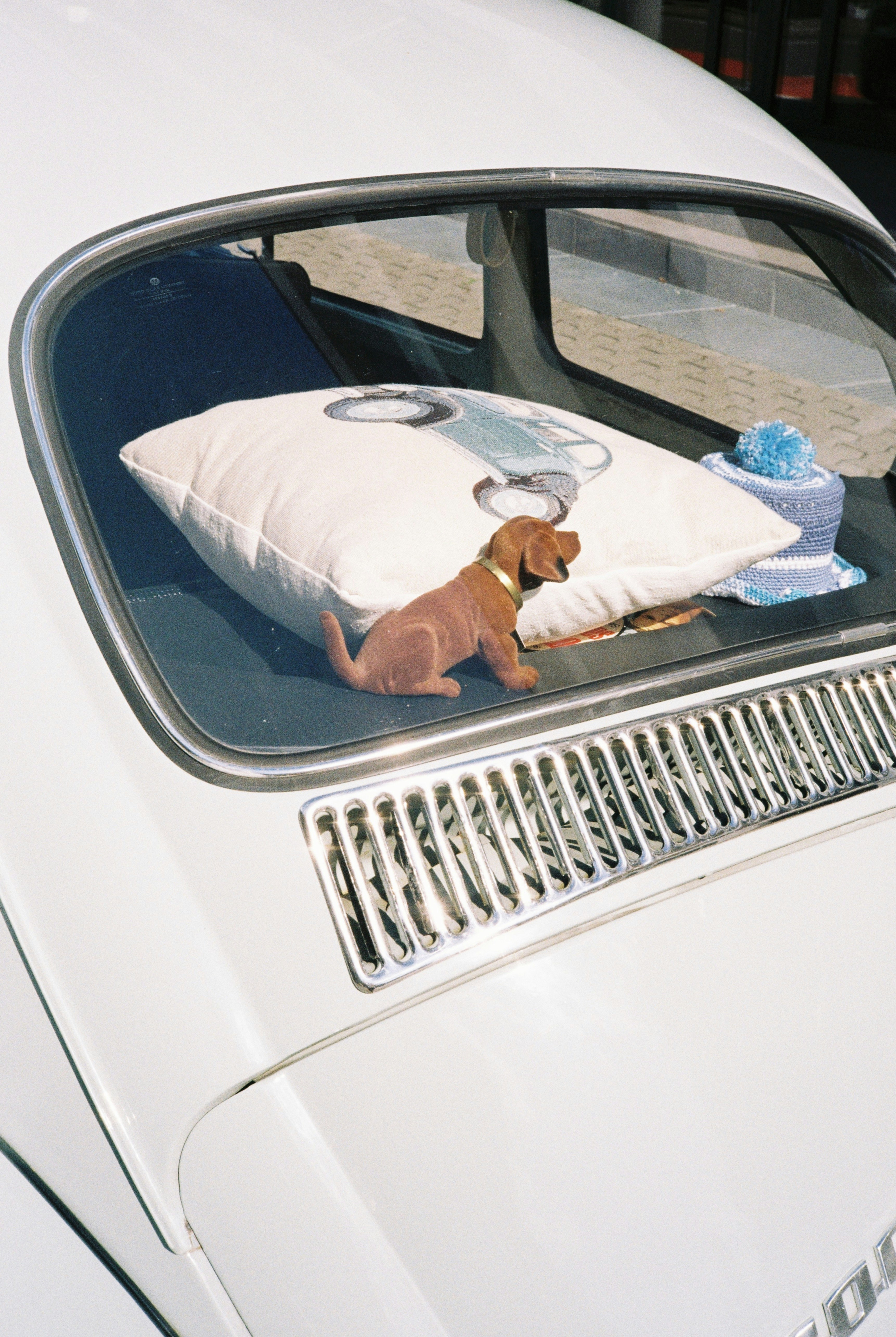 A small brown dachshund figurine beside a white pillow on a car rear shelf