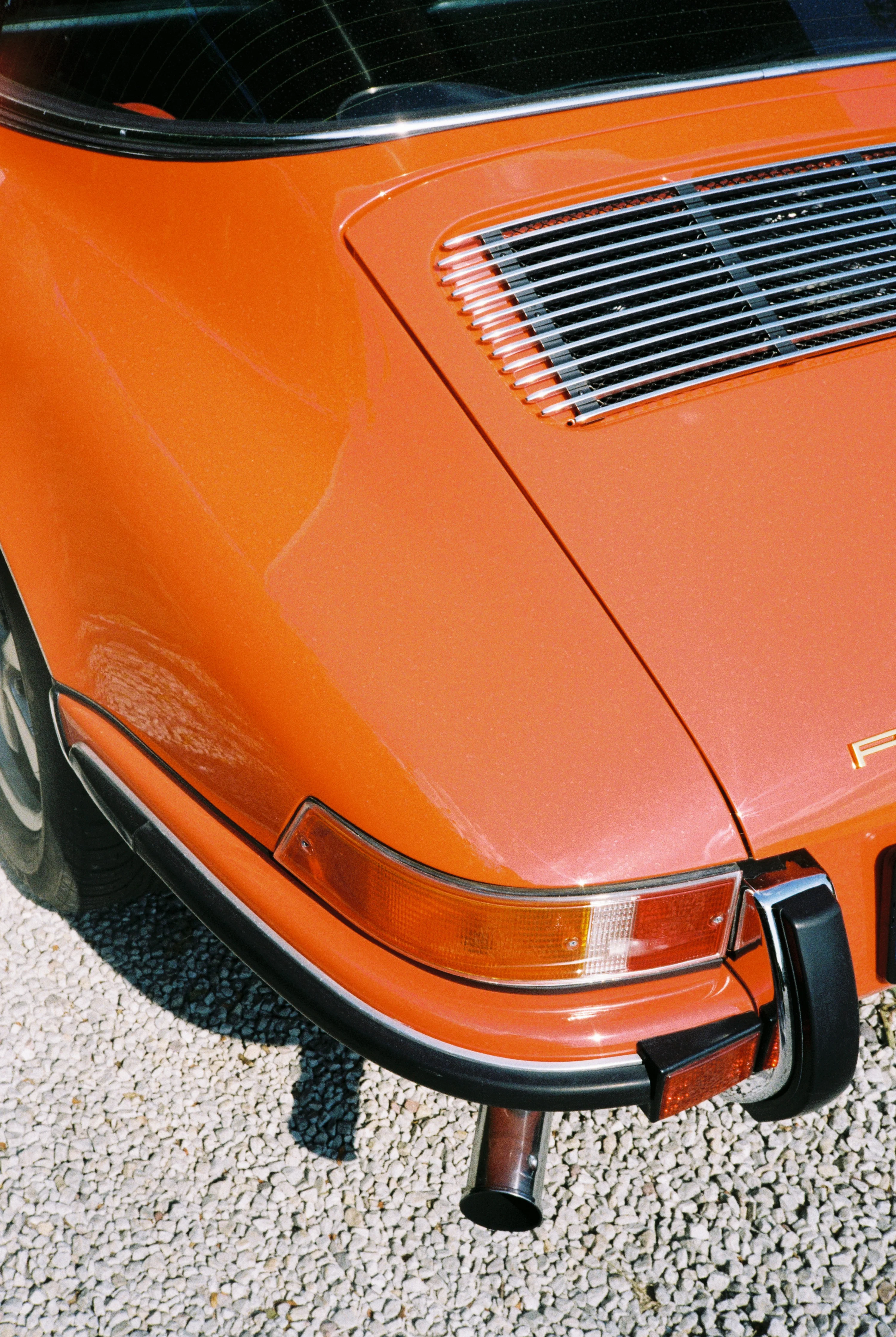 The rear quarter of an orange vintage sports car on a gravel surface