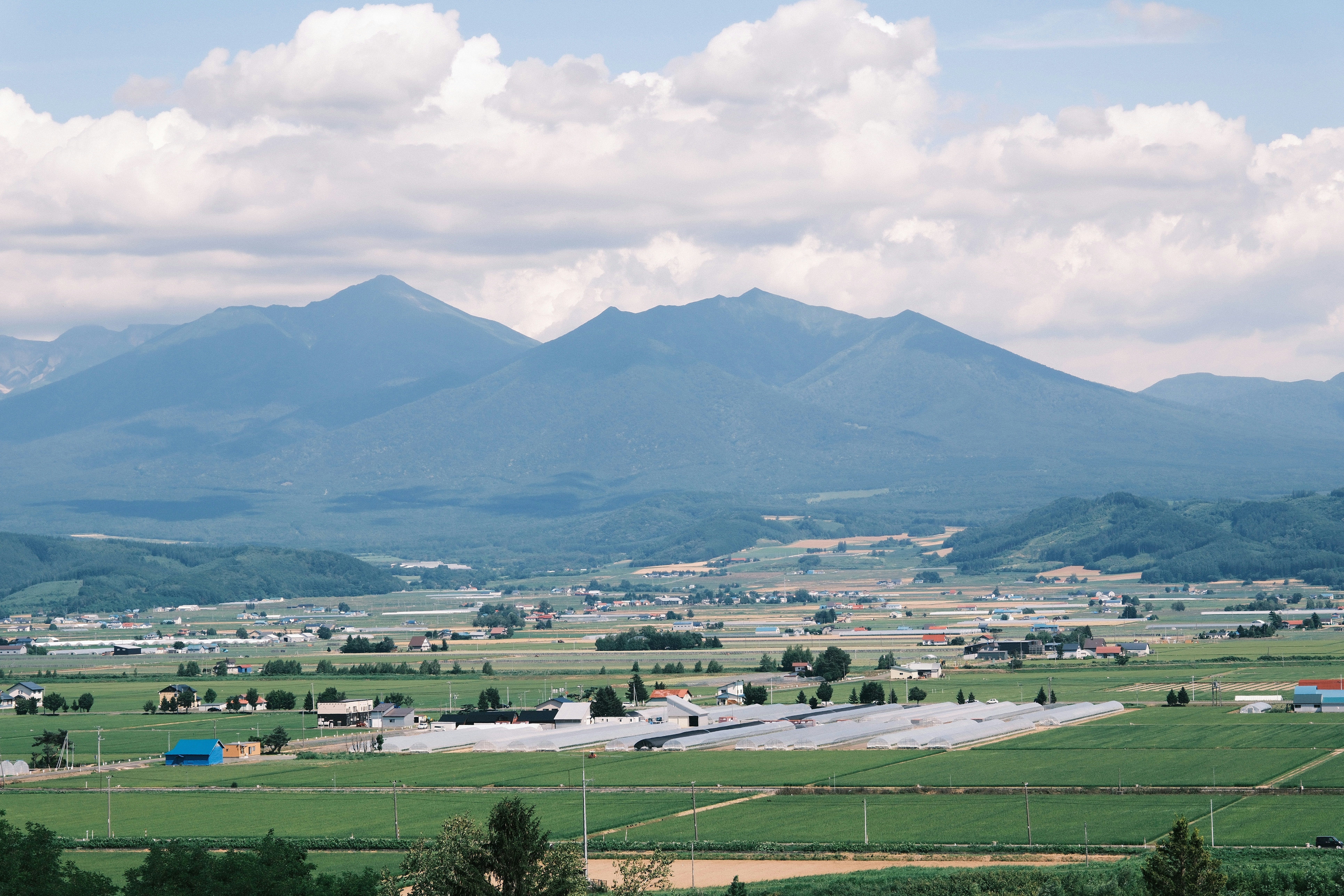 Green fields and greenhouses in a valley below distant blue mountains under clouds