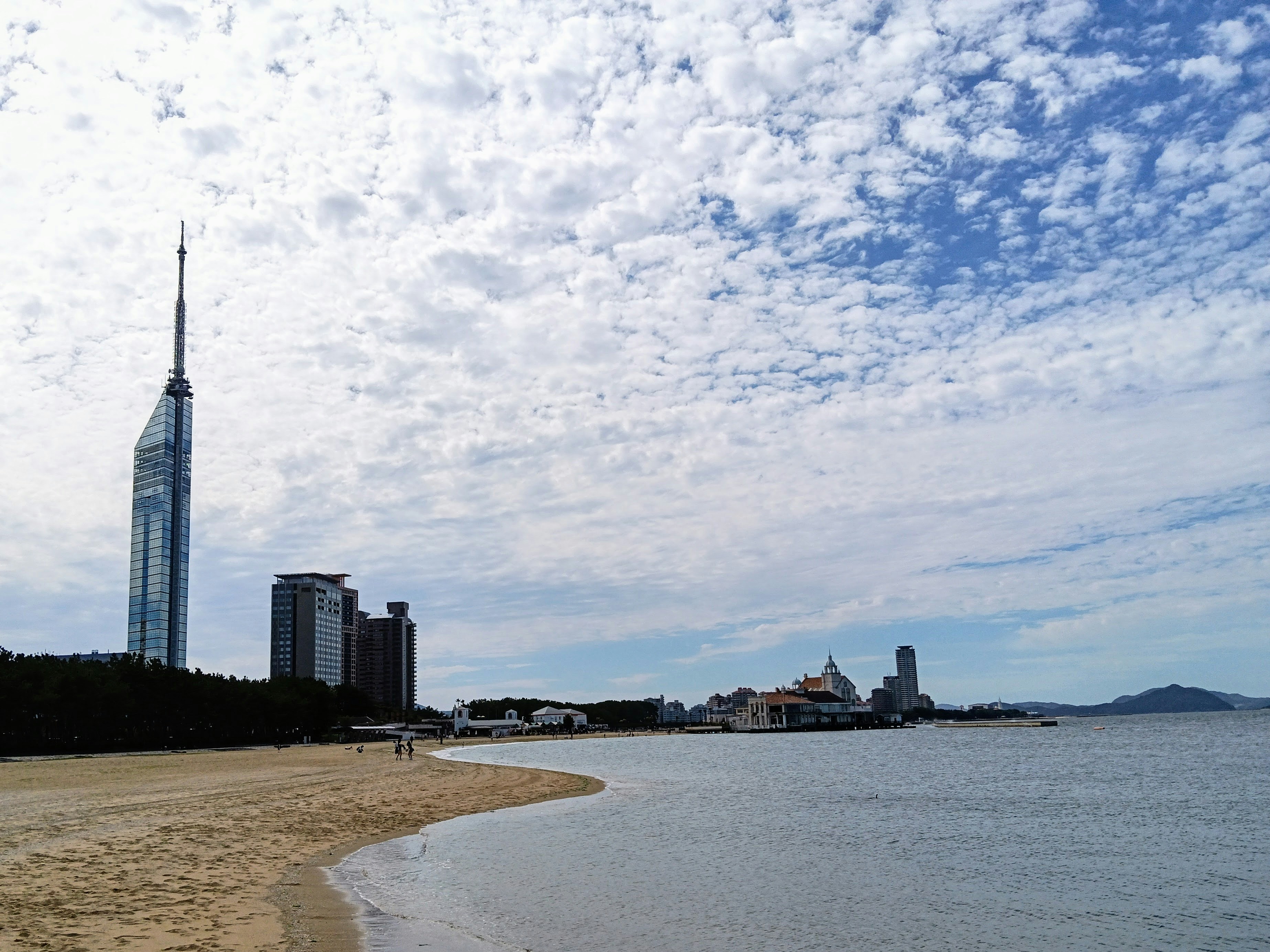 Fukuoka Tower rising above a sandy beach and calm water under a cloudy sky