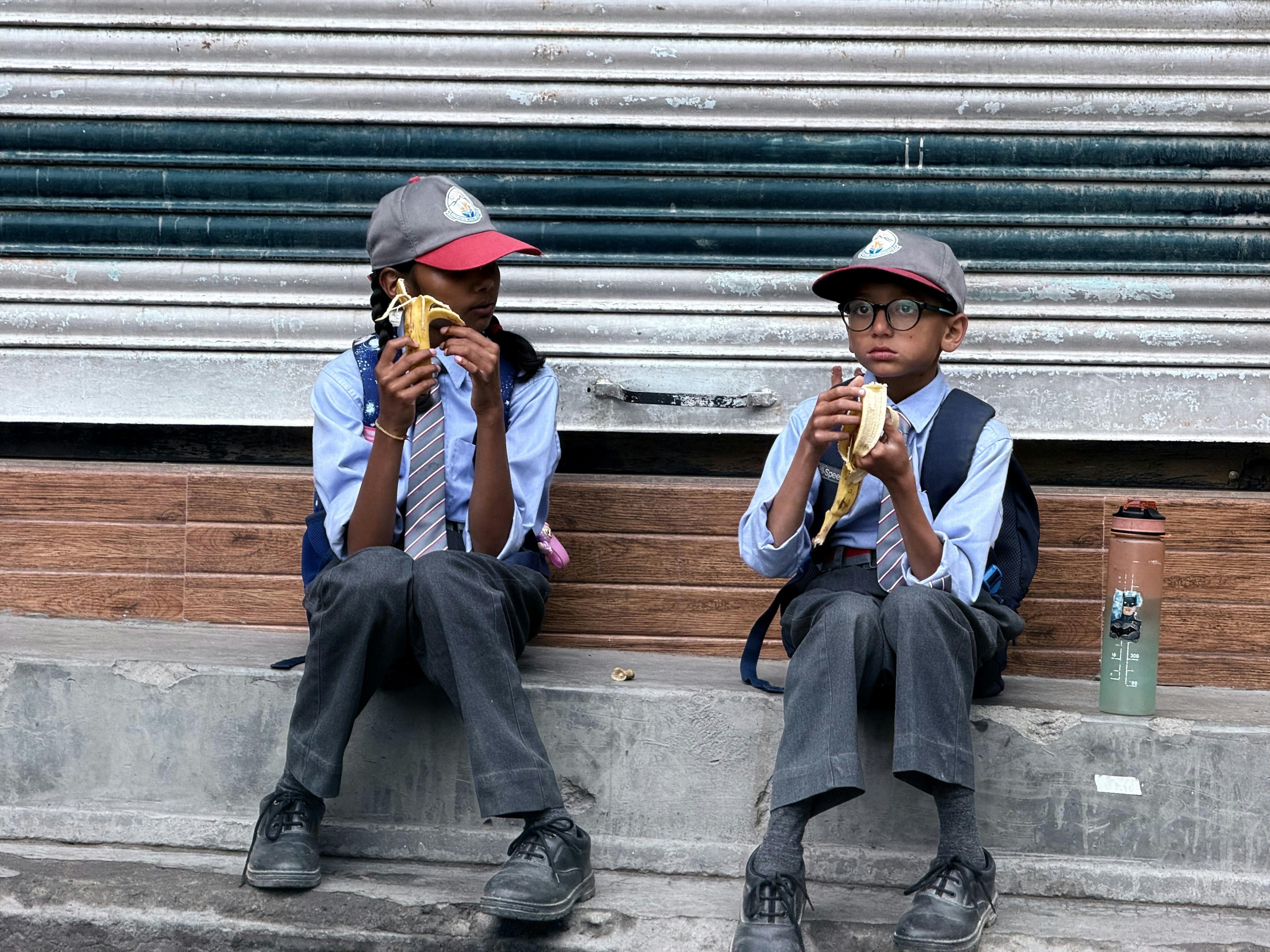 Two students in school uniforms sitting on a step eating bananas