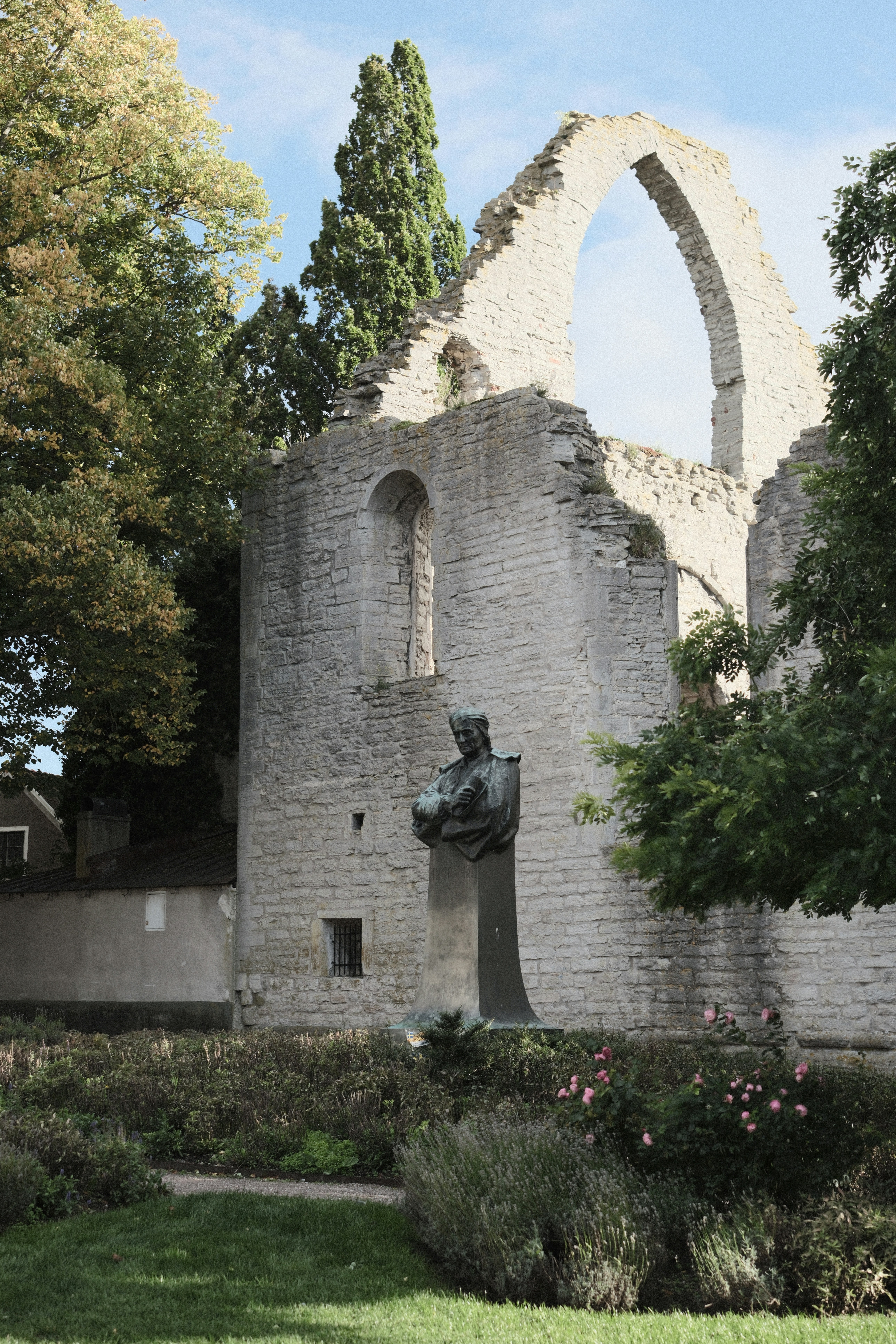 A bronze statue of a man in front of stone ruins and trees
