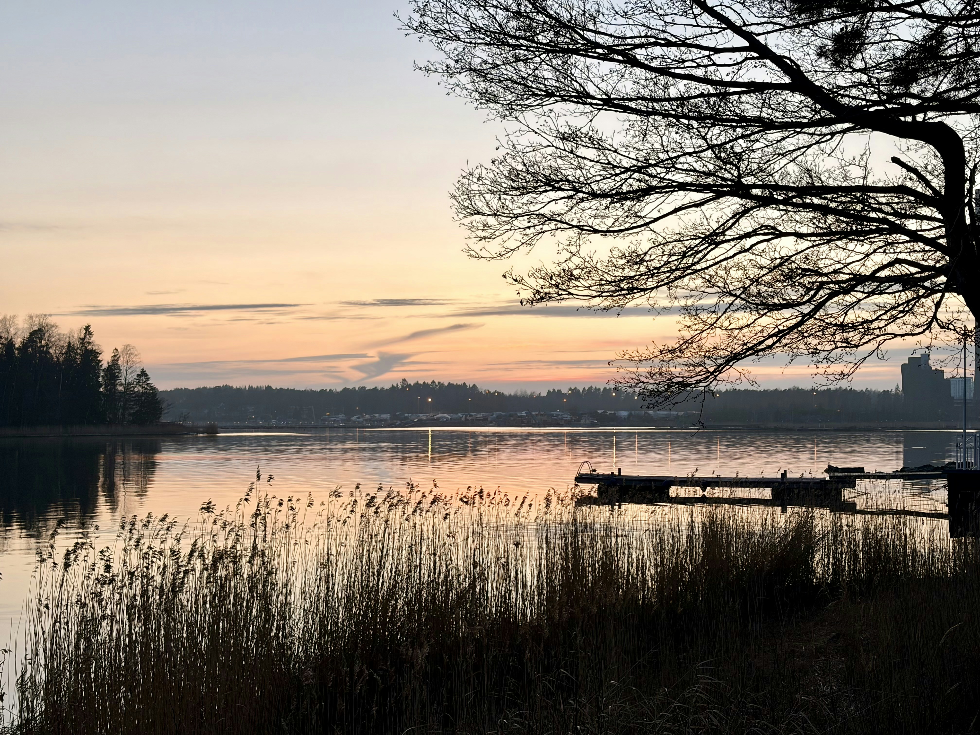 A wooden pier extending into a calm lake under a soft orange sky