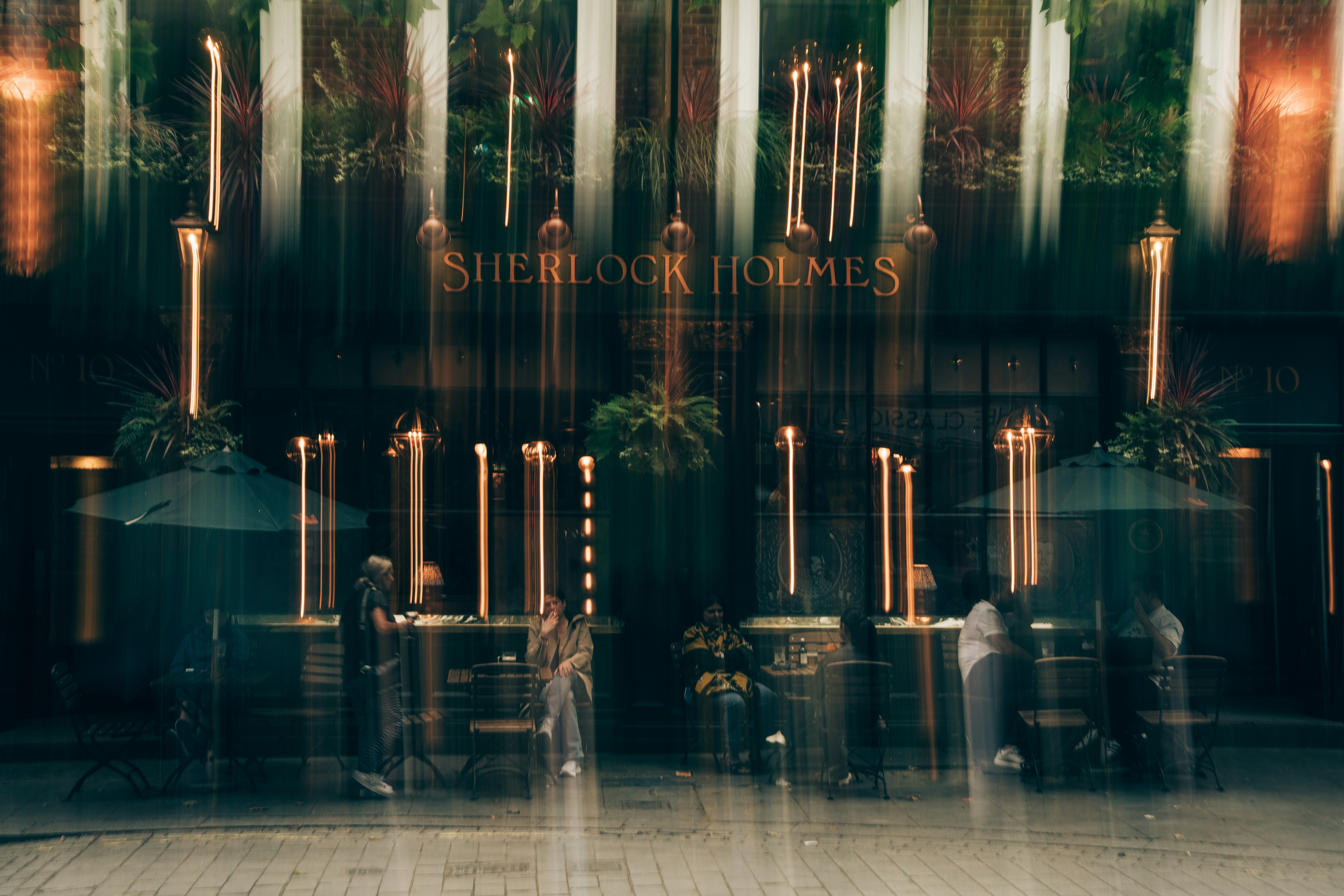 People sitting at tables outside the Sherlock Holmes pub with vertical light streaks