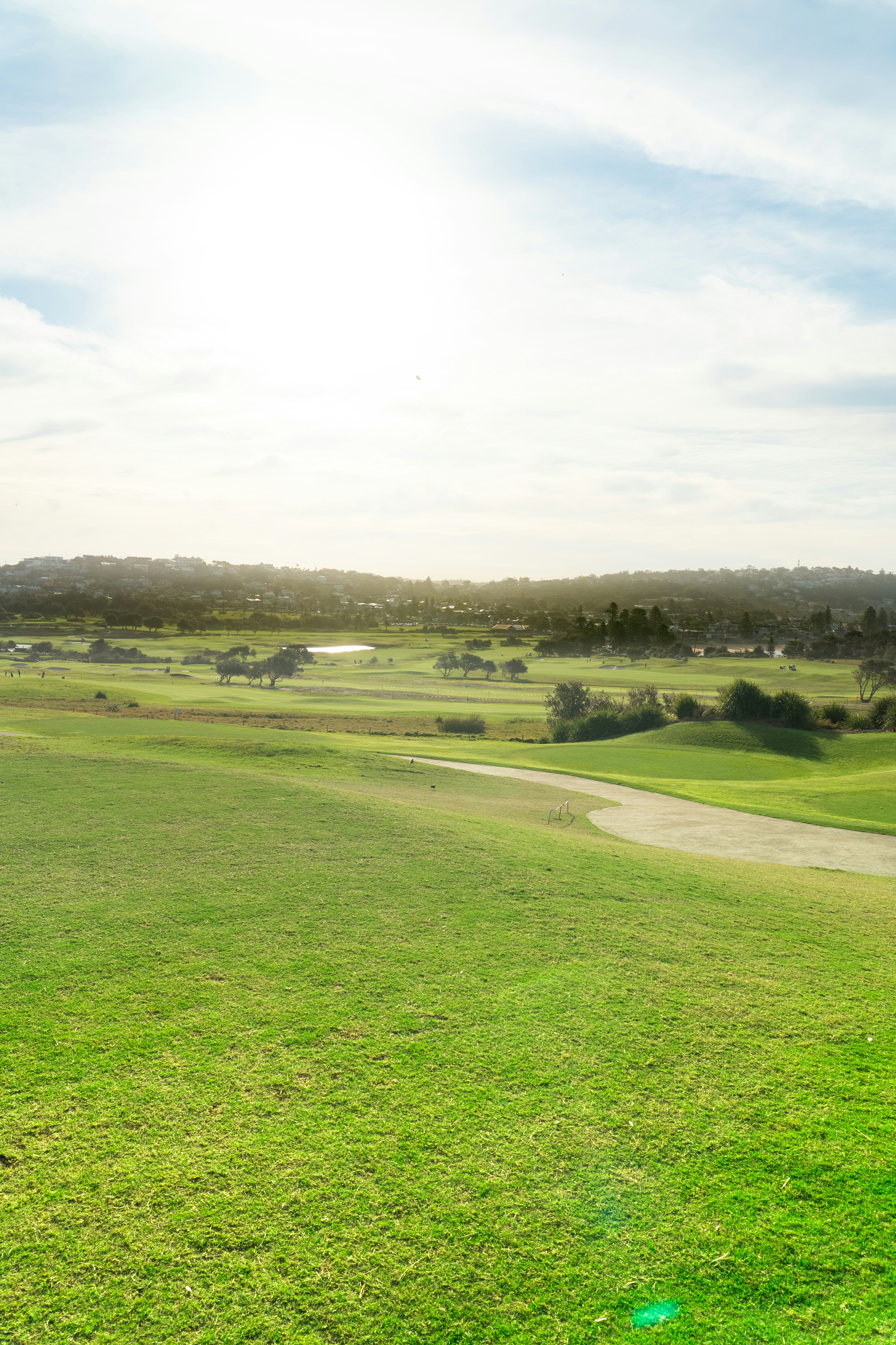 A wide golf course with green fairways under a bright hazy sky