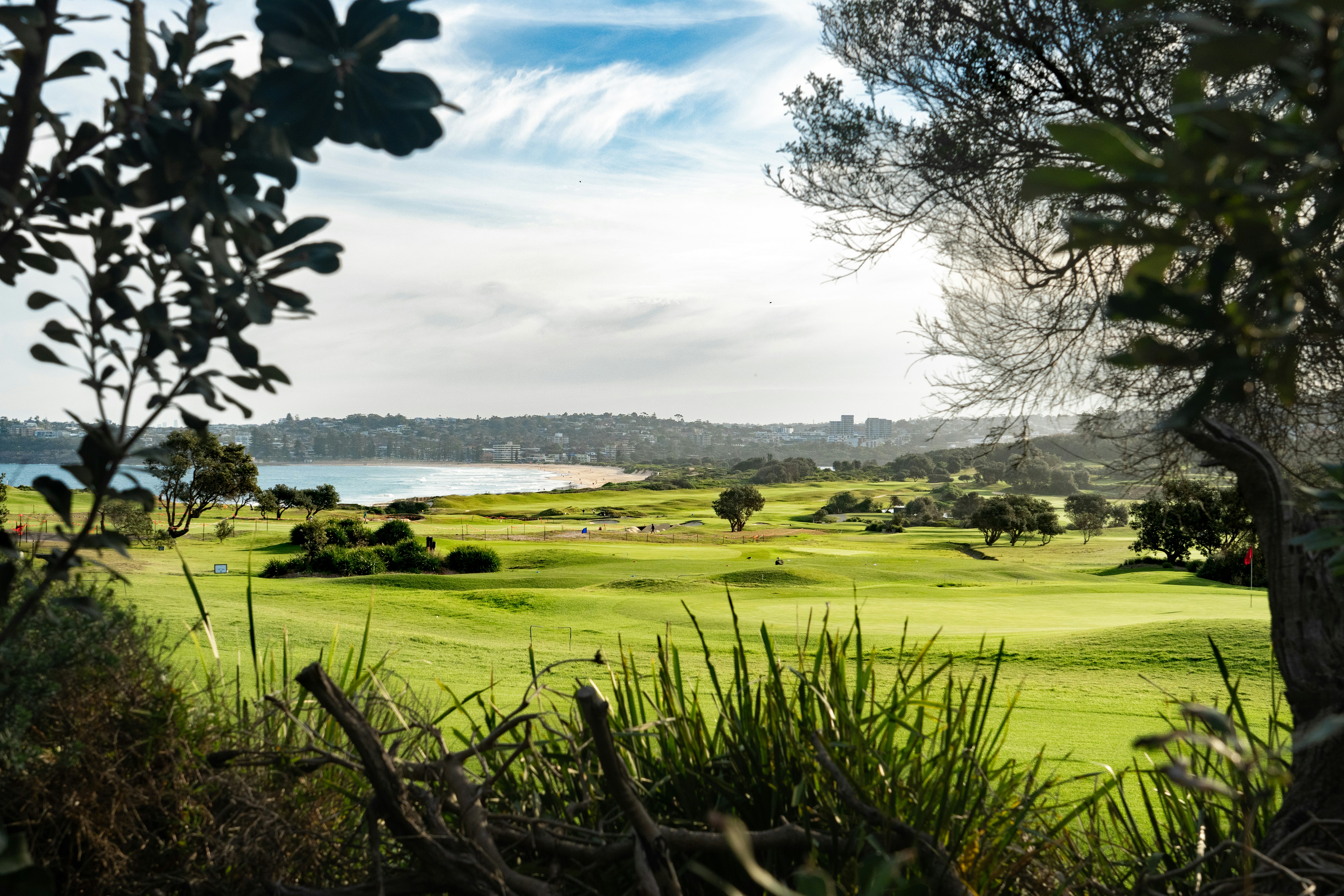 A green golf course beside a sandy beach and ocean under a blue sky