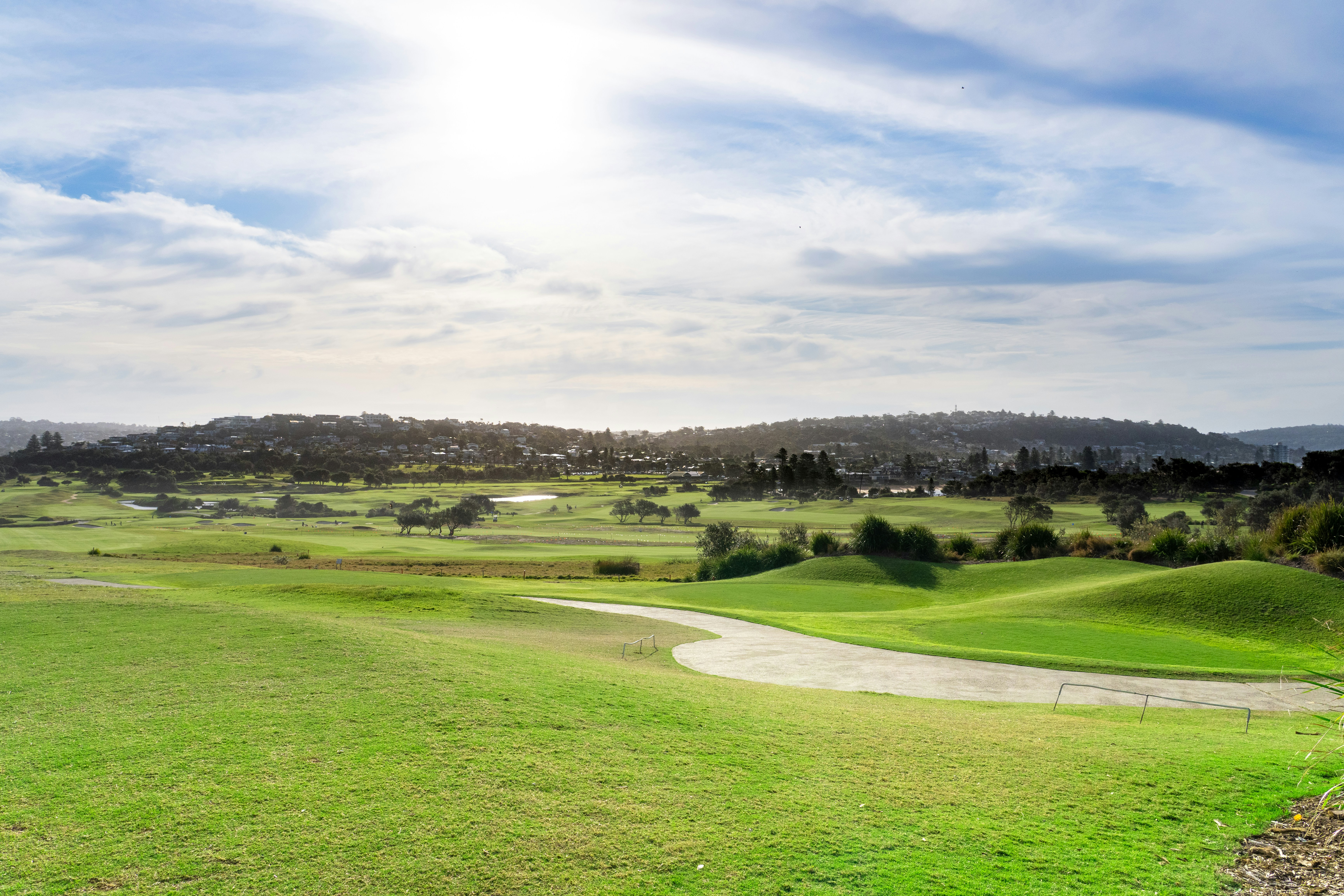 A golf course with rolling green fairways under a bright sky with low sun