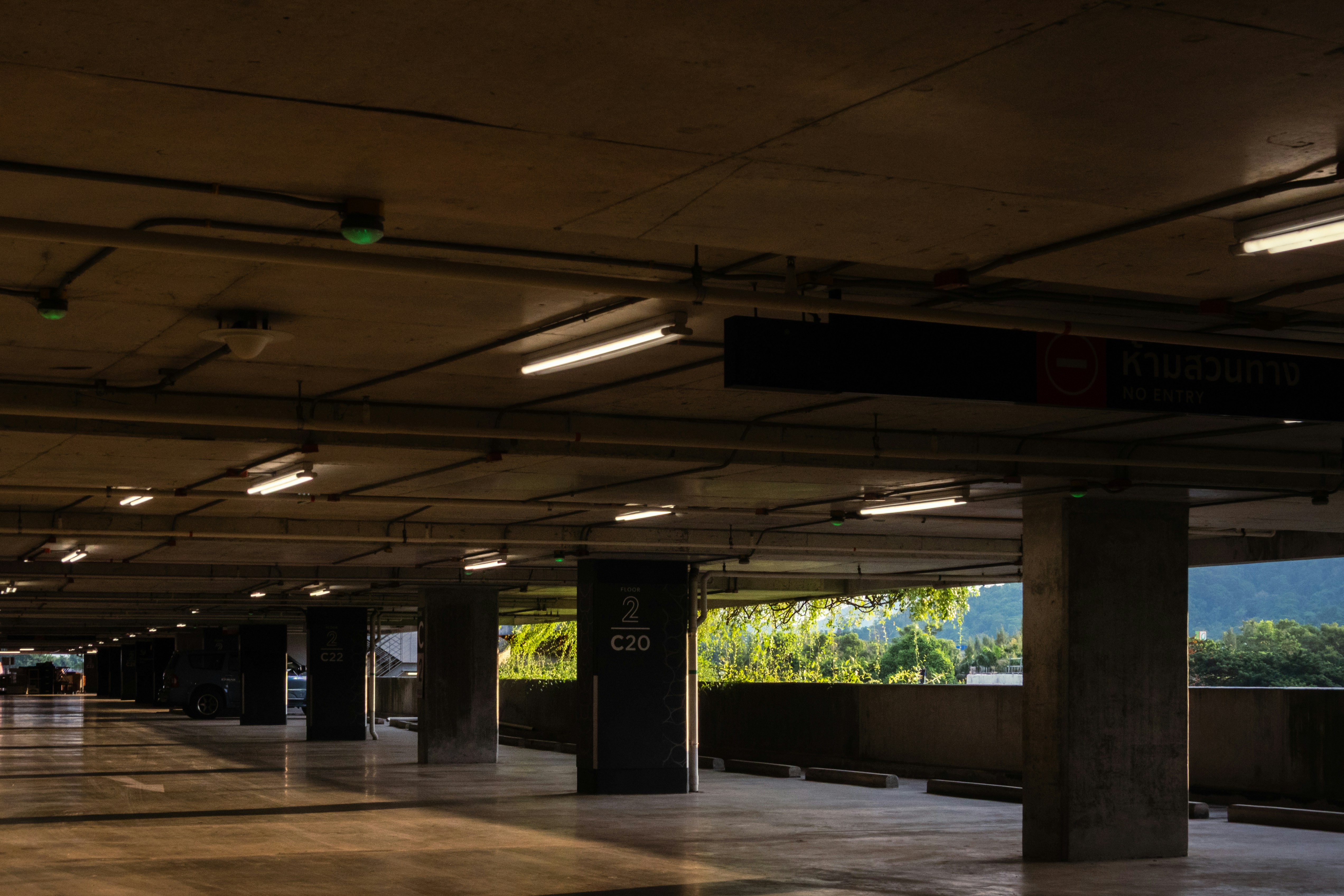 An empty concrete parking garage with fluorescent lights and a view of green trees