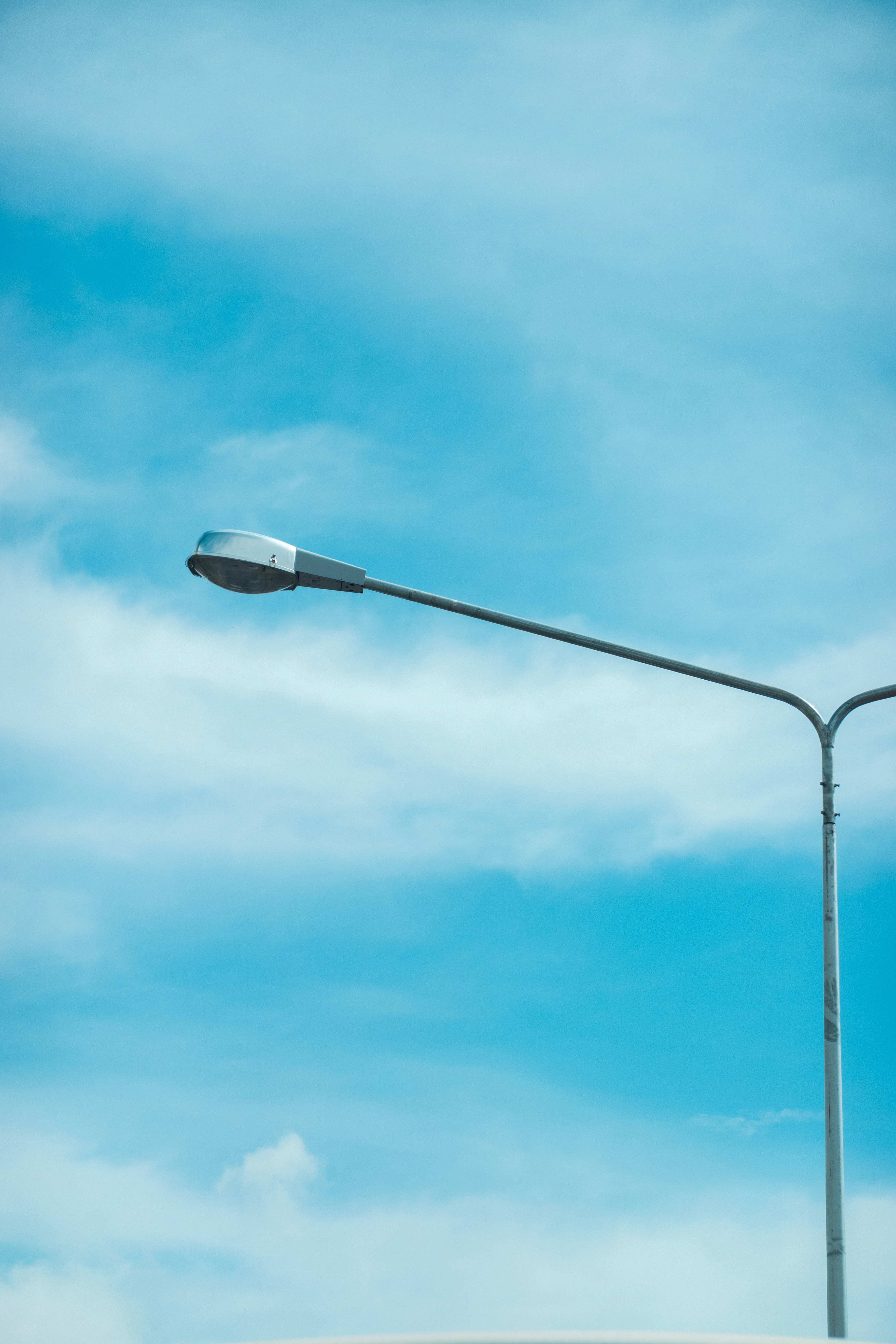 A metal street lamp against a bright blue sky with scattered white clouds